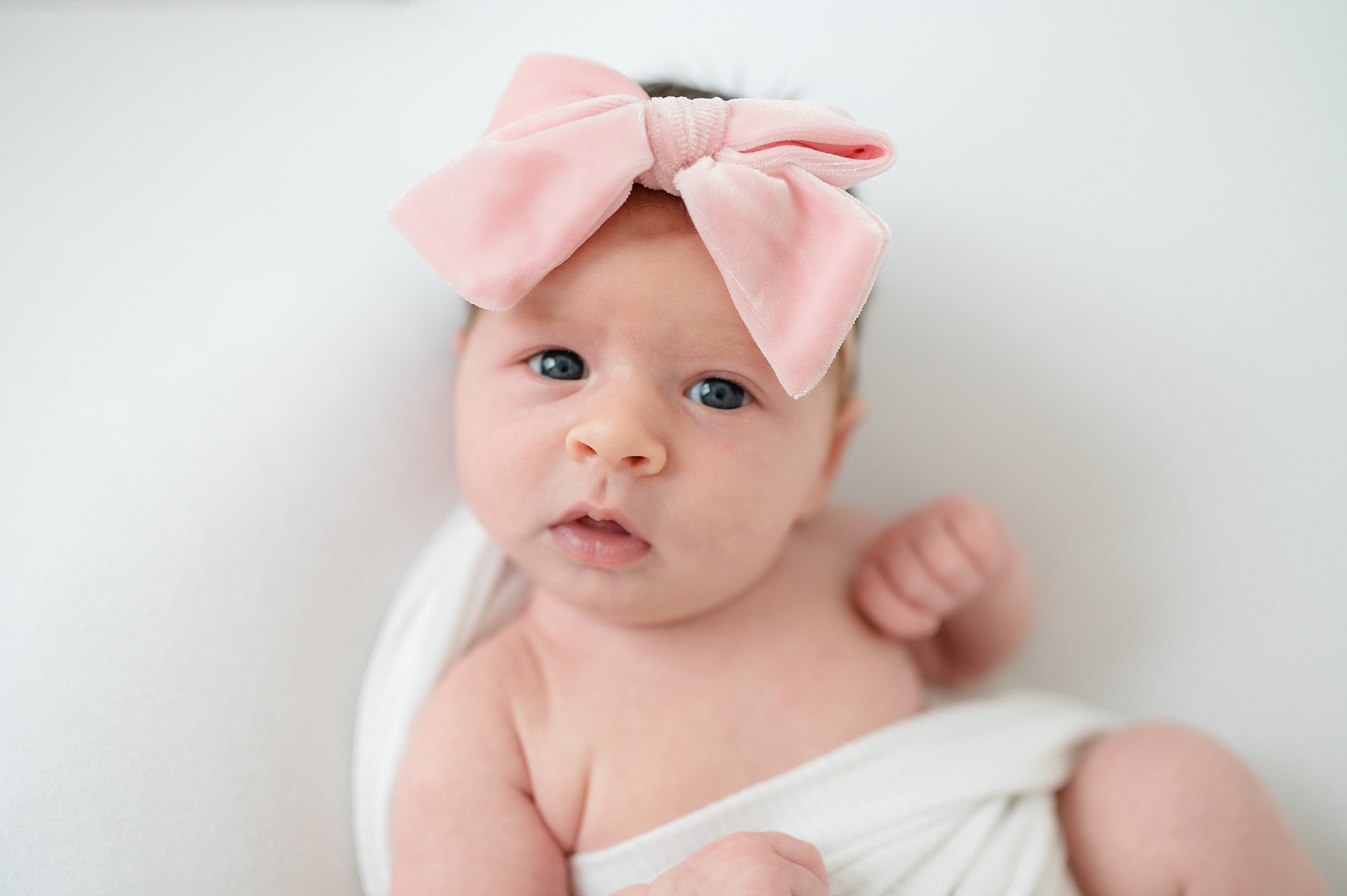 infant baby girl in pink bow surrounded by white taken by Lindsey Dutton Photography, a Dallas newborn photographer
