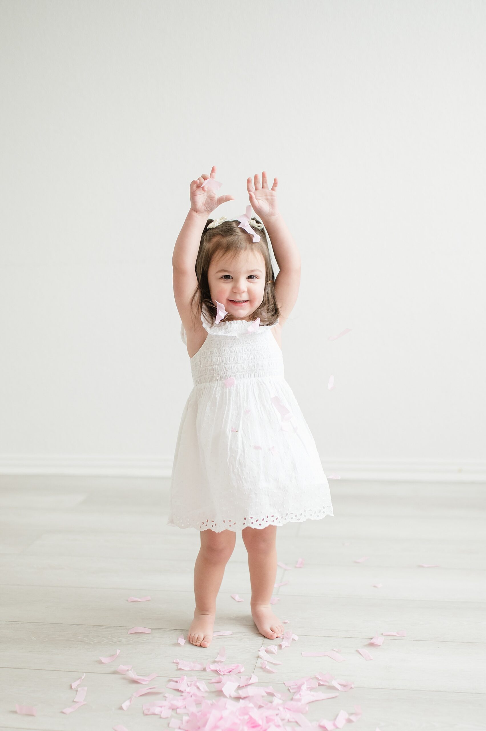 little girl in white dress plays in pink confetti from gender reveal photo session taken by Lindsey Dutton Photography, a Dallas Maternity photographer
