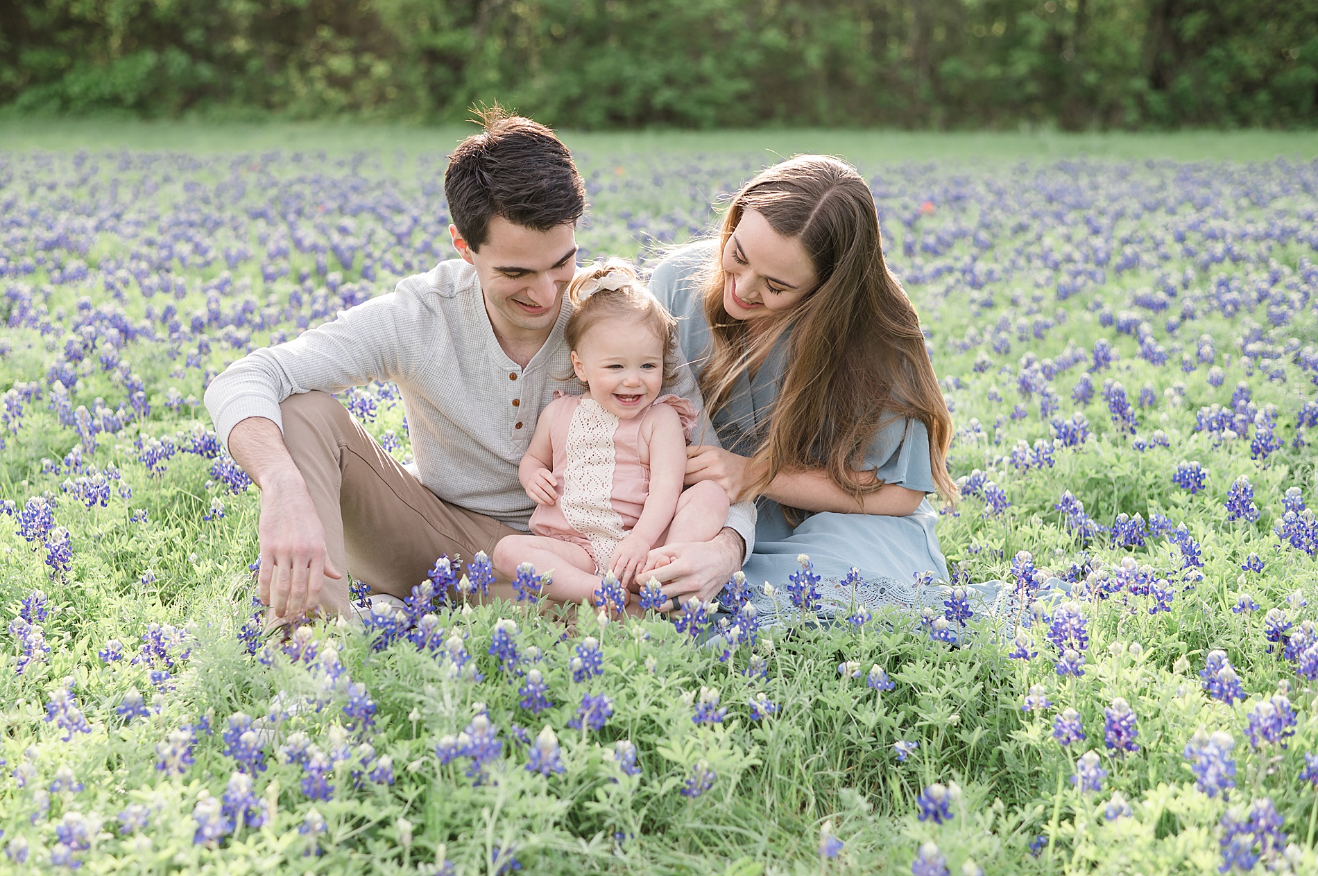 parents sit with their little girl in a field of bluebonnets photographed by Lindsey Dutton Photography, a Dallas family photographer