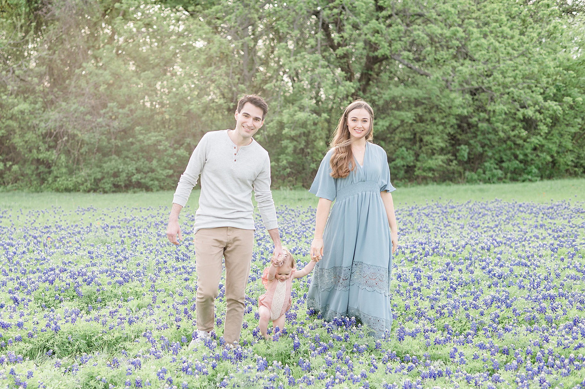 family of three hold hands as they walk through field of bluebonnets in Dallas TX photographed by Lindsey Dutton Photography, a Dallas family photographer