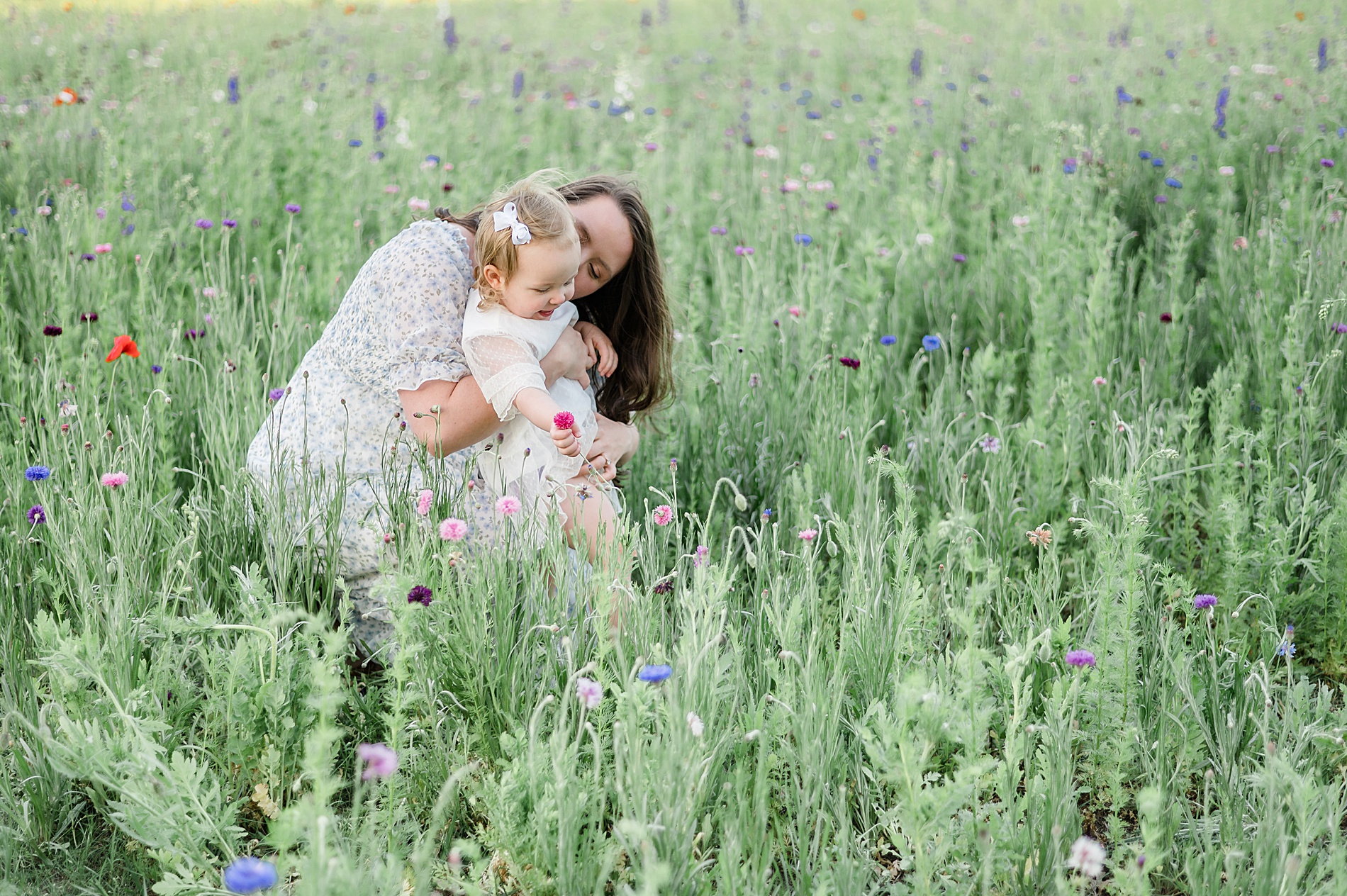 mom sits with daughter in field of wildflowers photographed by Lindsey Dutton Photography, a Dallas family photographer