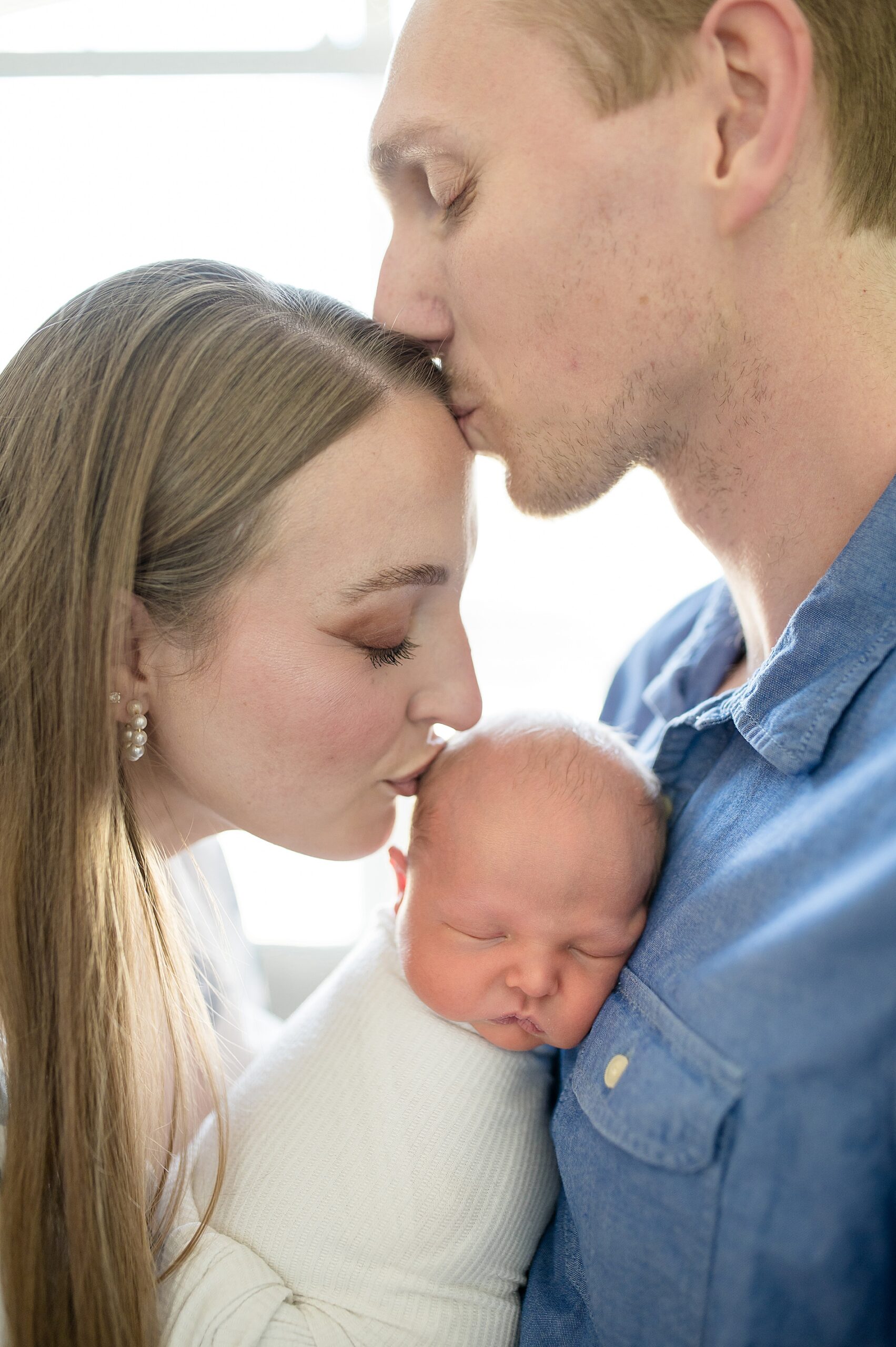 newborn sleeps as parents kiss their forehead taken by Lindsey Dutton Photography, a Dallas newborn photographer
