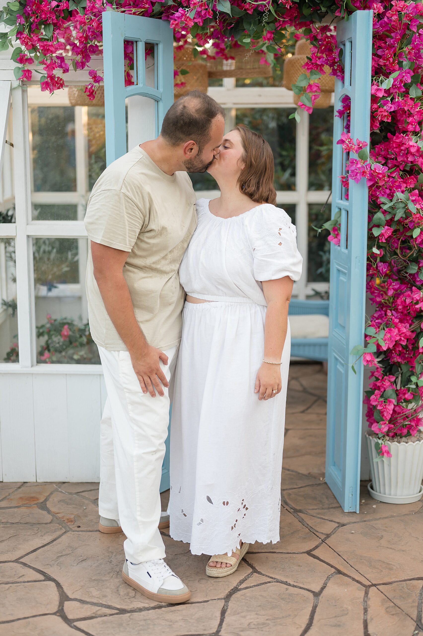 summer couples portraits in front of greenhouse decorated with pink flowers taken by Lindsey Dutton Photography, a Dallas Family photographer
