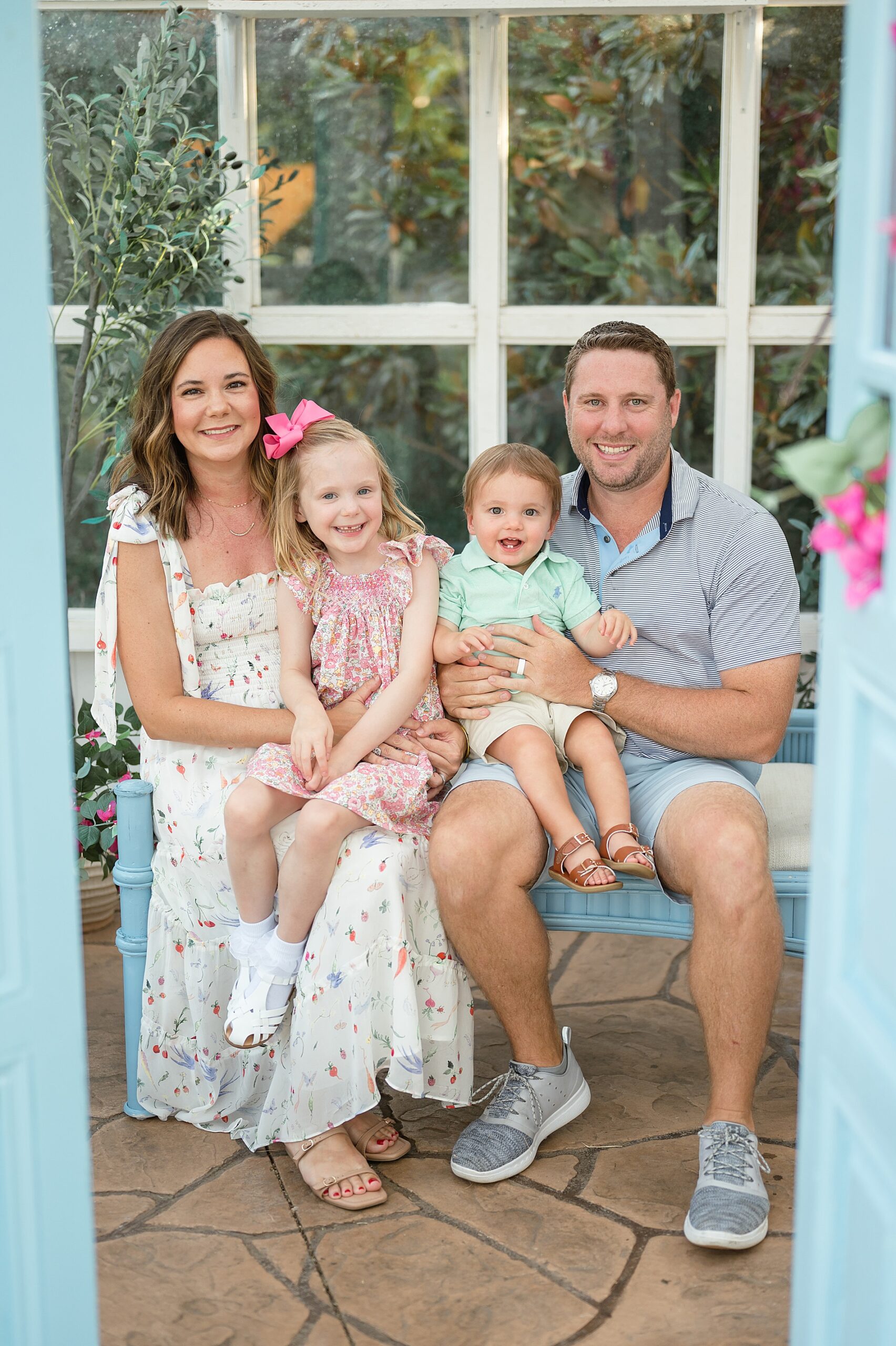 family of four sit together on bench in greenhouse taken by Lindsey Dutton Photography, a Dallas Family photographer