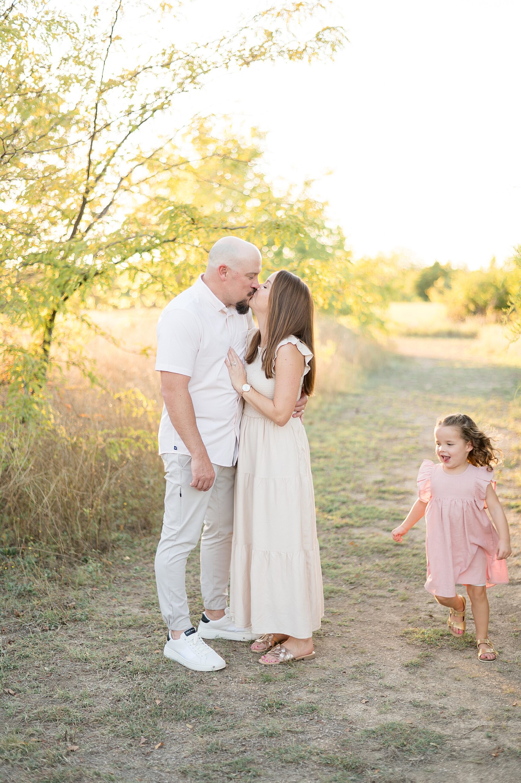 parents kiss as little girl runs around them taken by Lindsey Dutton Photography, a Dallas Family photographer | Choosing the Right Photography Package for Your Family