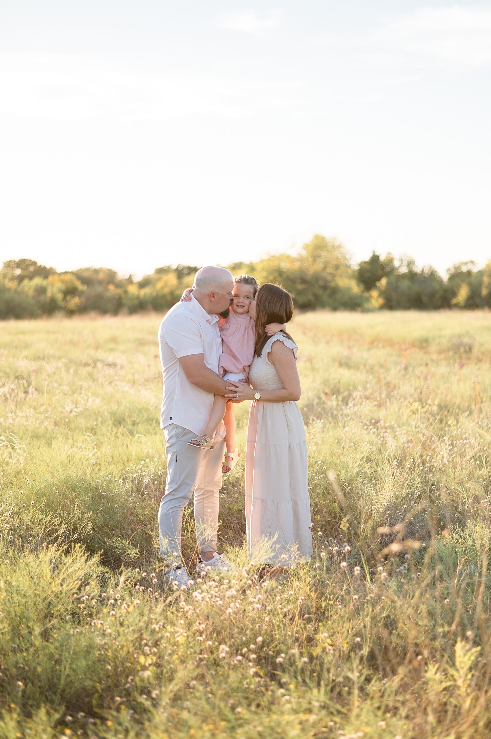 golden hour family photos parents kiss daughter's cheek | Choosing the Right Photography Package for Your Family | photographed by Lindsey Dutton Photography, a Dallas Family photographer
