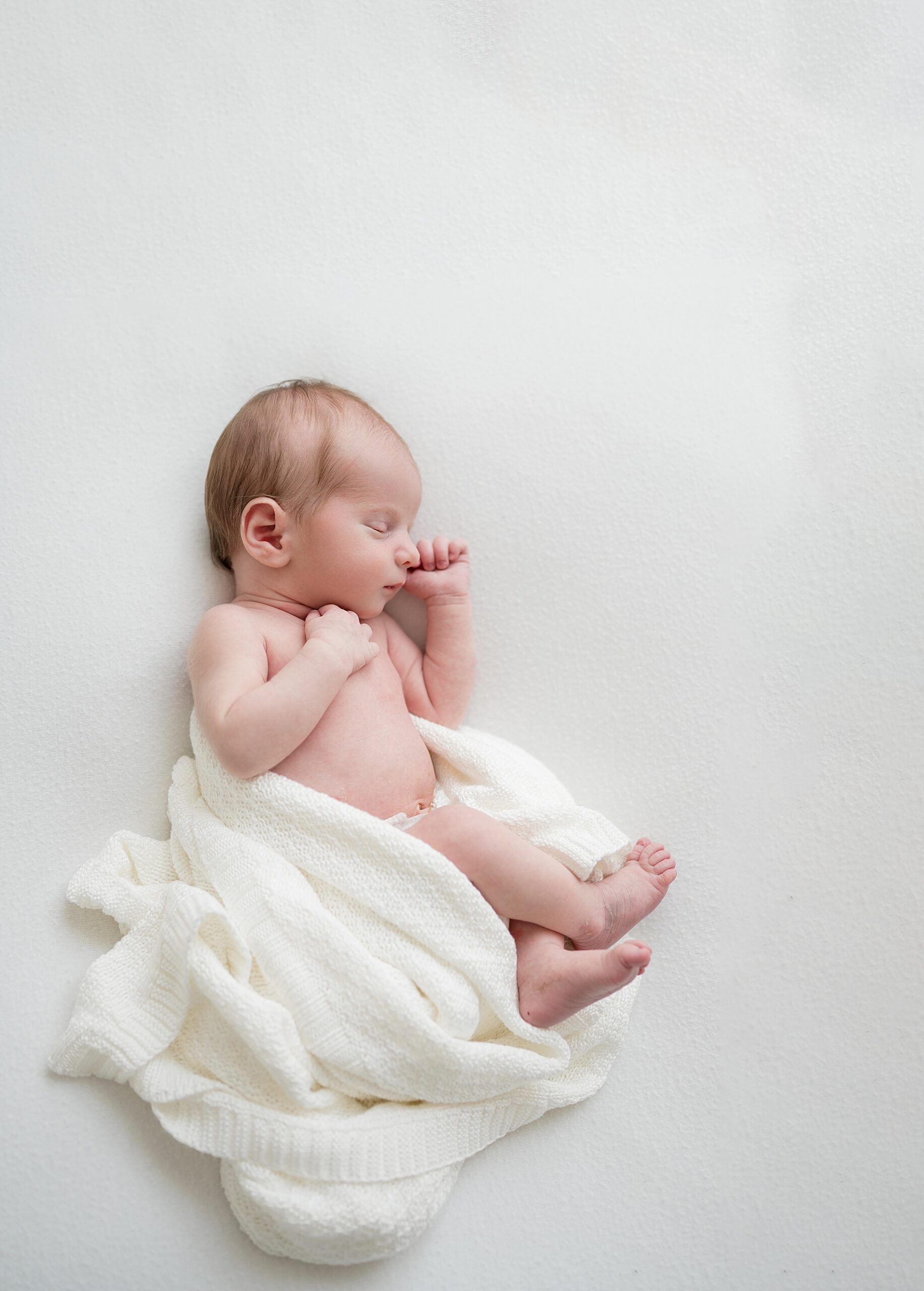 newborn sleeps on side with white blanket around him in this Simple Baby-Led Newborn Photography session