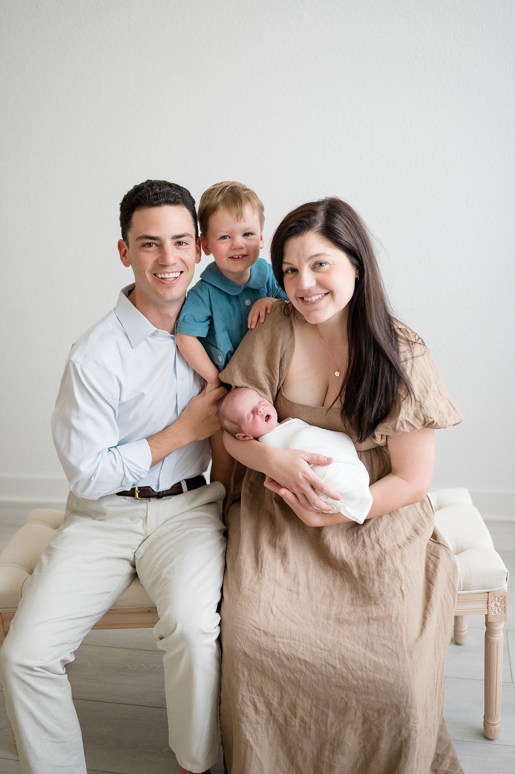 family of four sit together on bench by Little Elm Tx newborn photographer