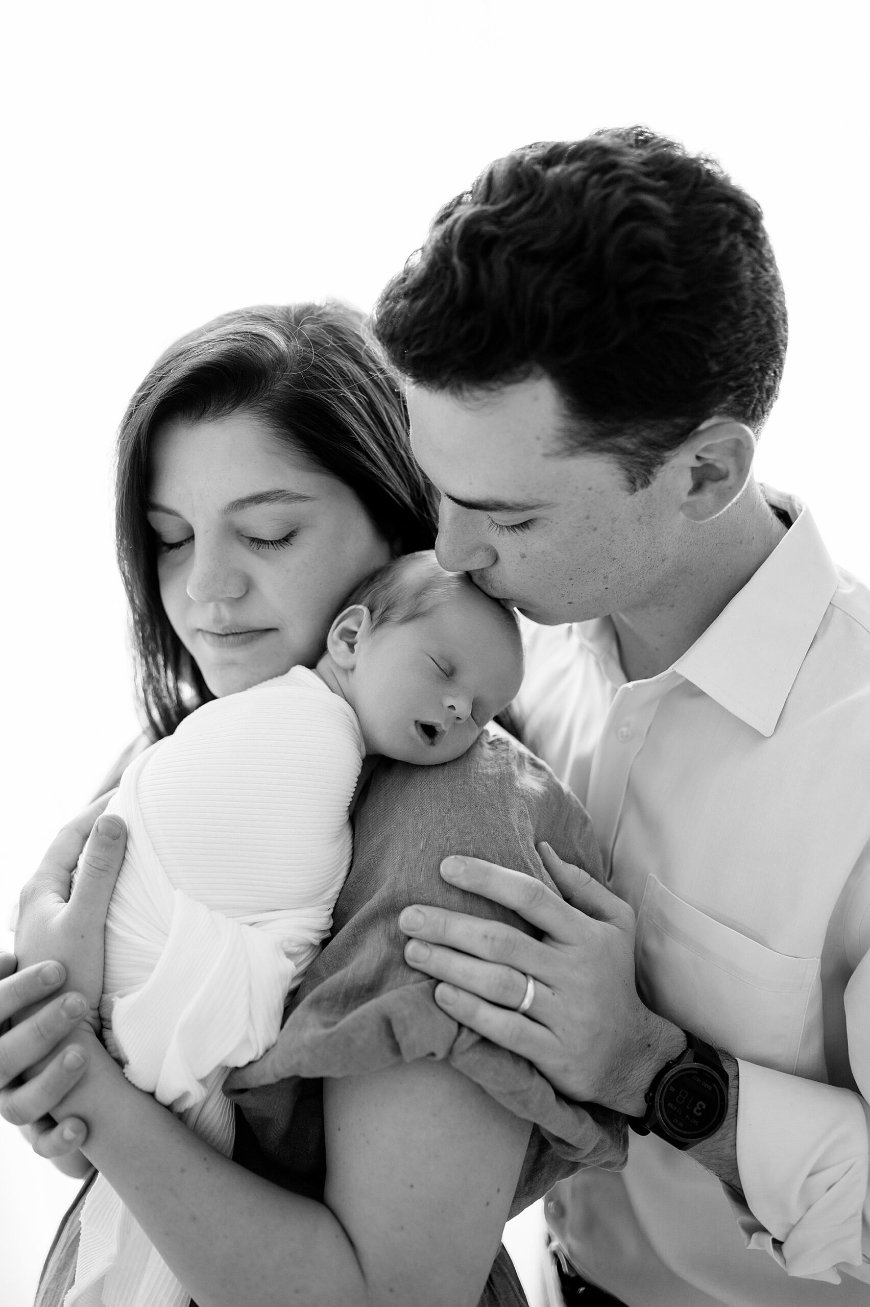 dad kisses newborn's head while resting in mom's arms | Newborn photographer in Plano, TX