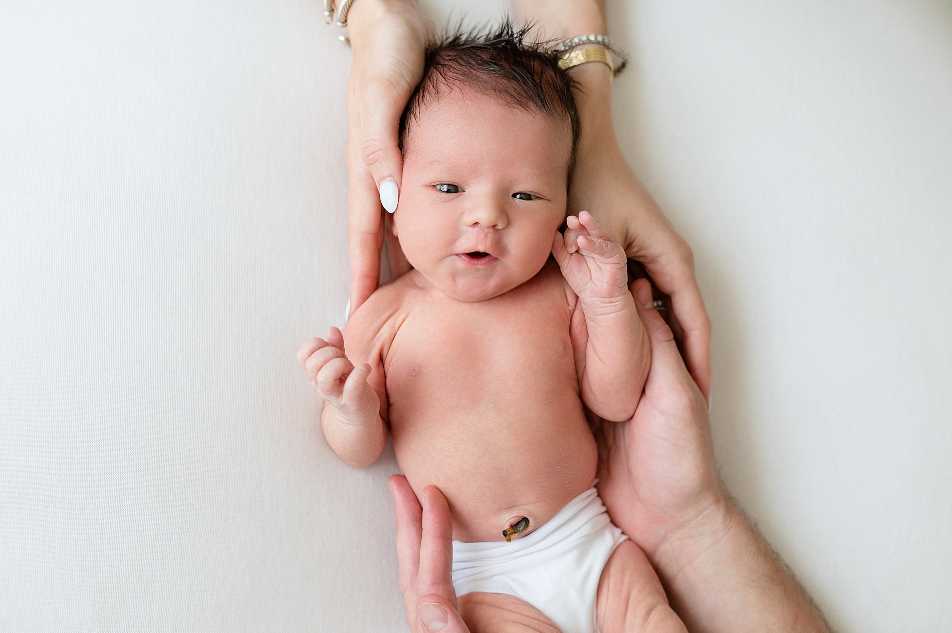 newborn with parents hands wrapped around him