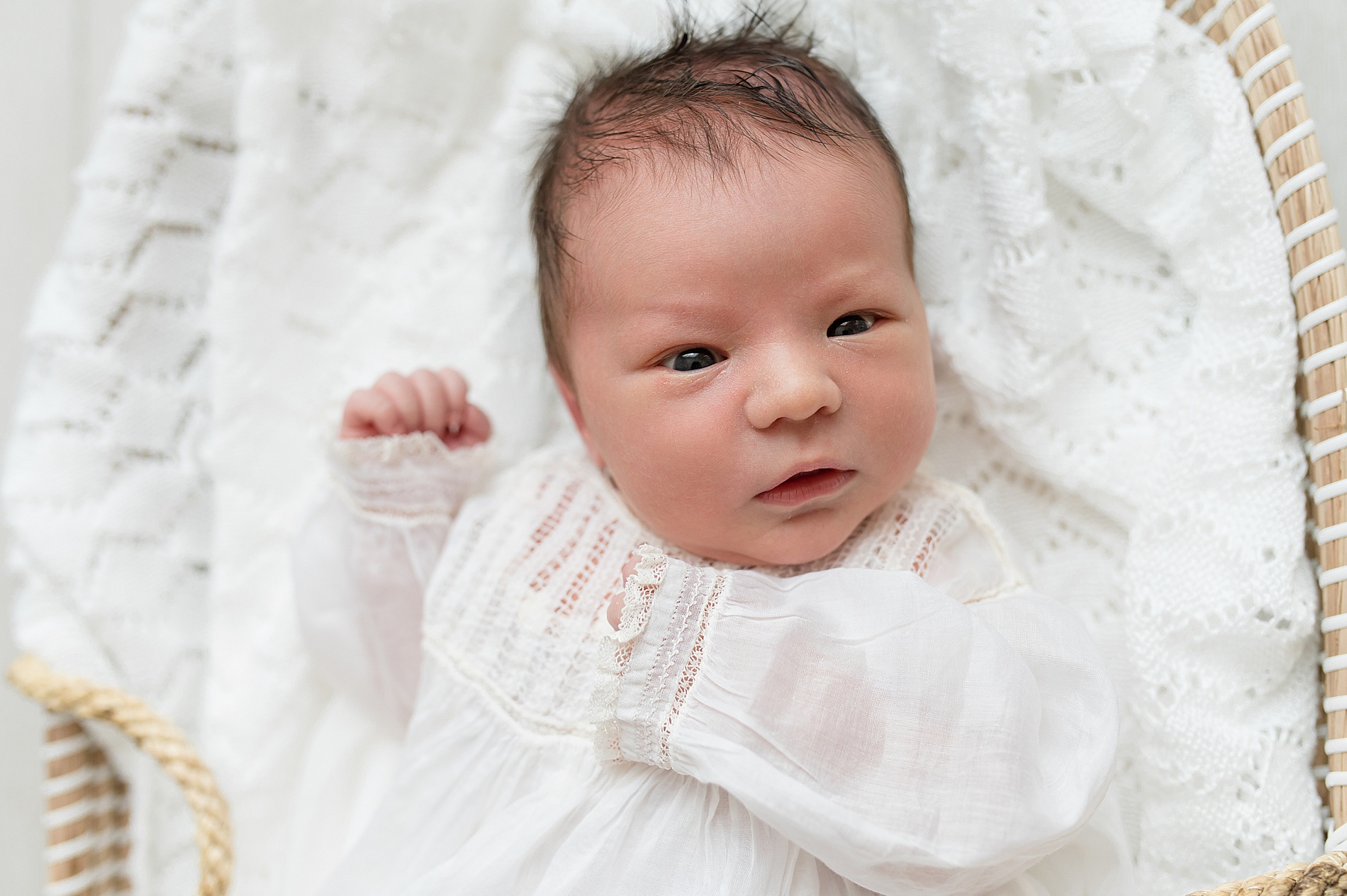 newborn in white outfit in bassinet