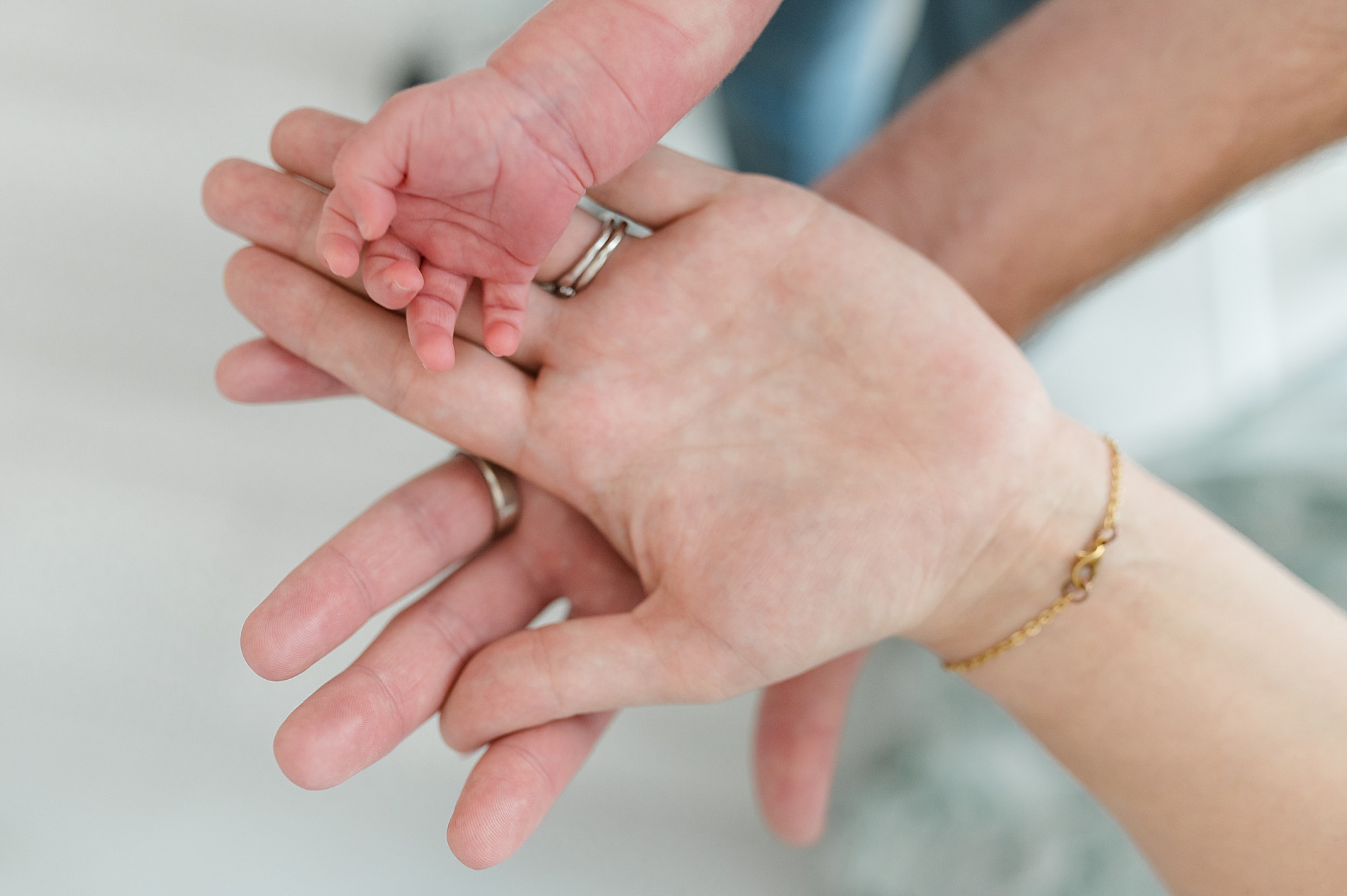 parents hands with newborn's tiny hand in the middle