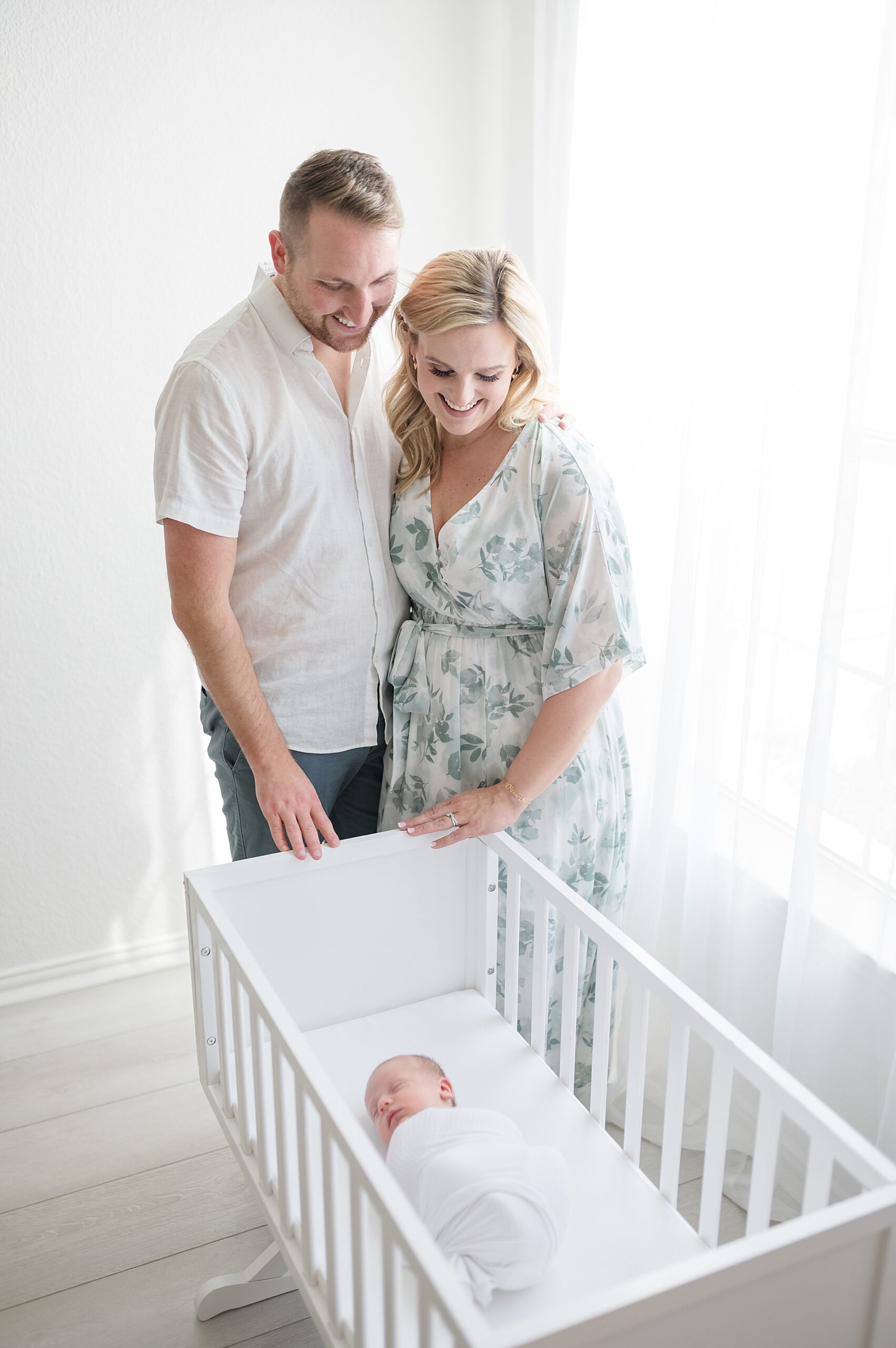 new parents look at newborn sleeping in crib