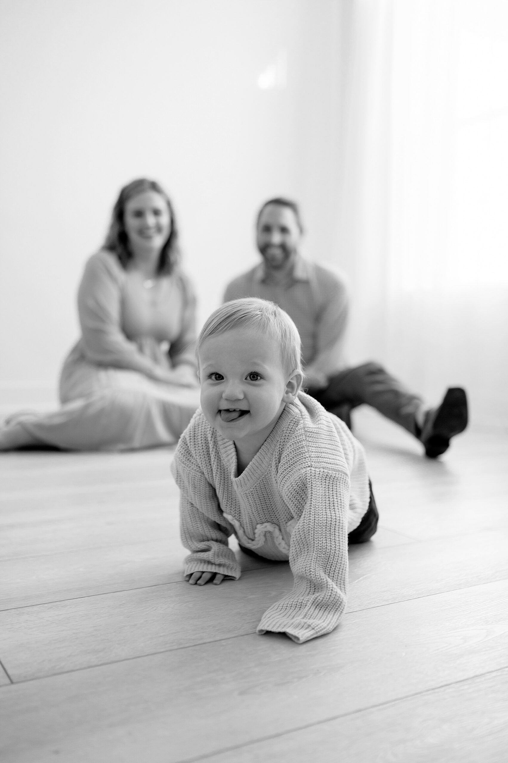 candid family photos of one year old crawling with parents watching lovingly.
