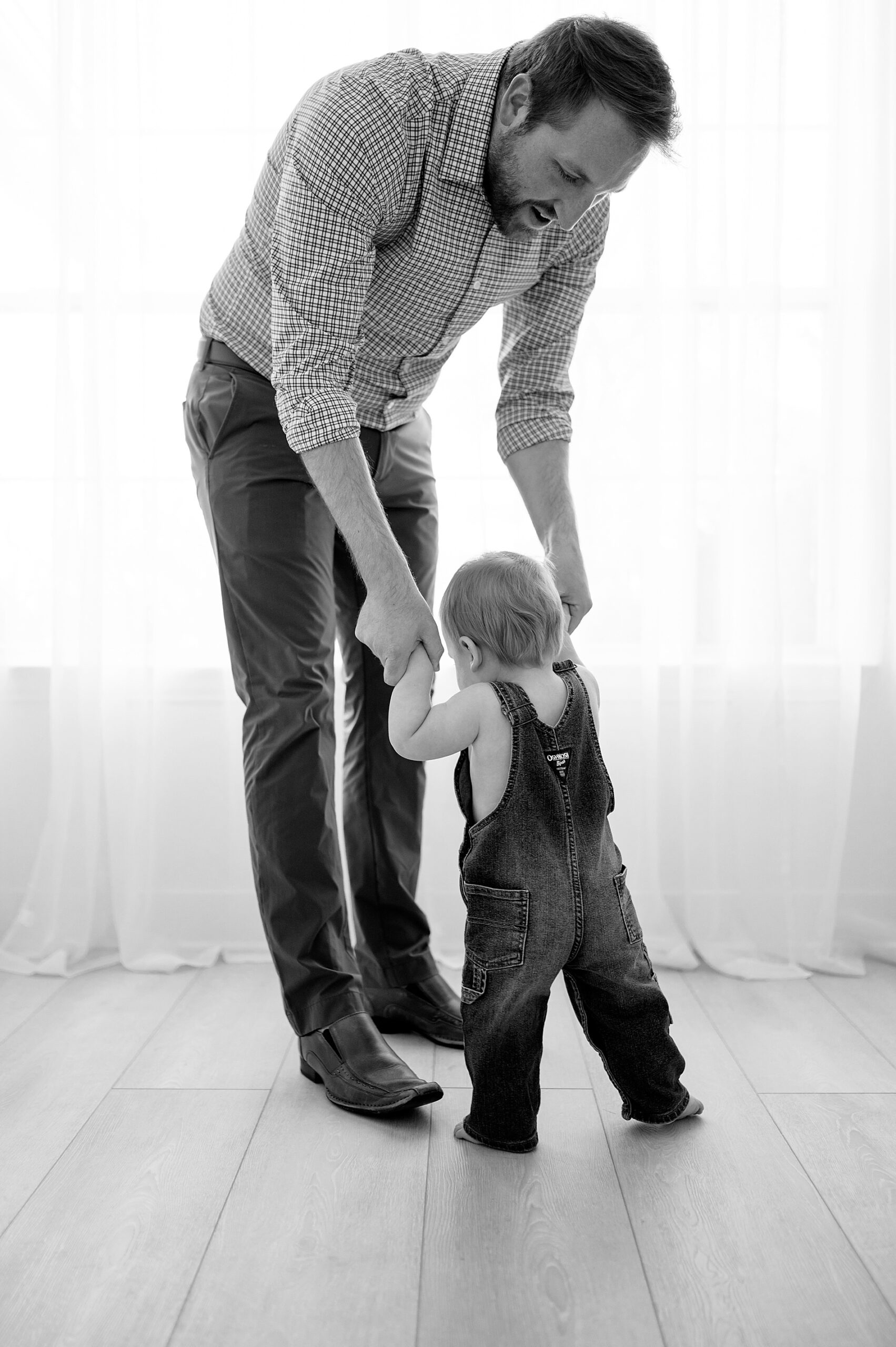 dad holds baby's hands as he tried to walk during one year session as part of my First Year Collection