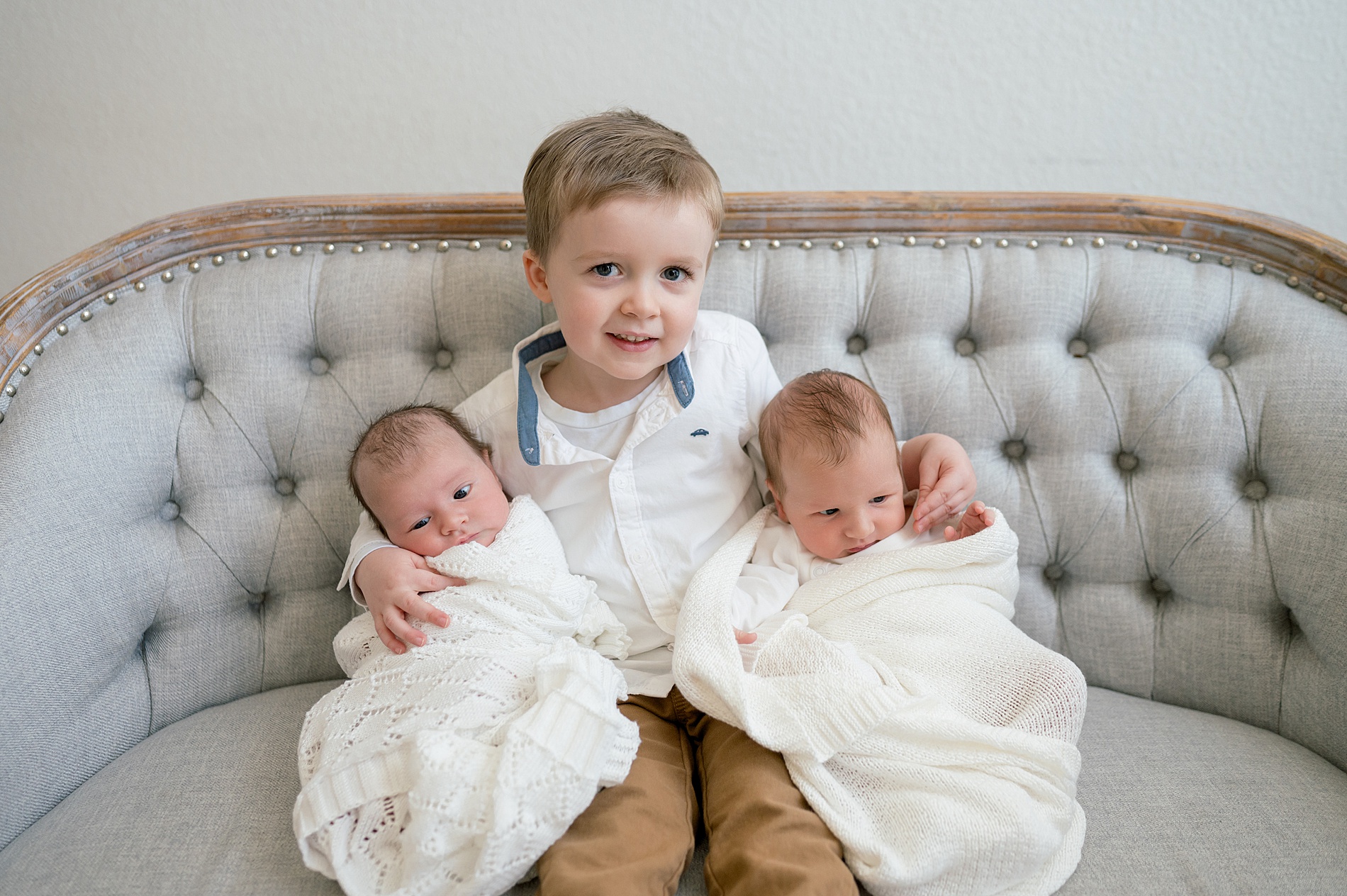 big brother holds twin siblings on couch