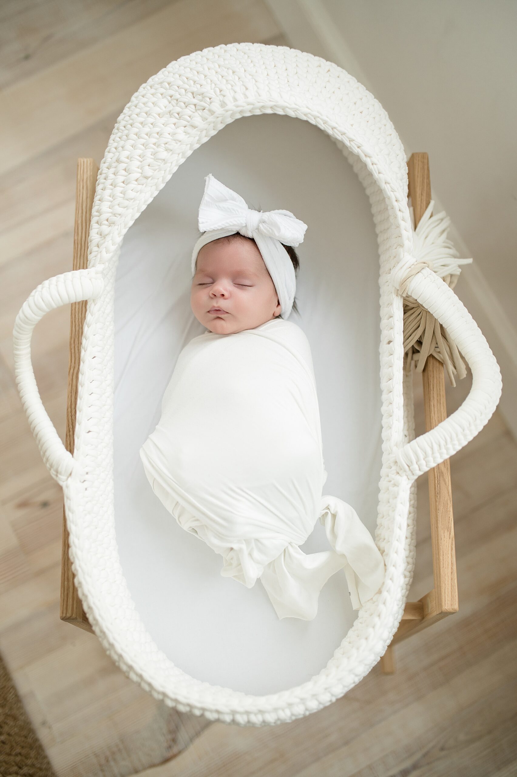 newborn baby girl wrapped in white blanket laying in bassinet 