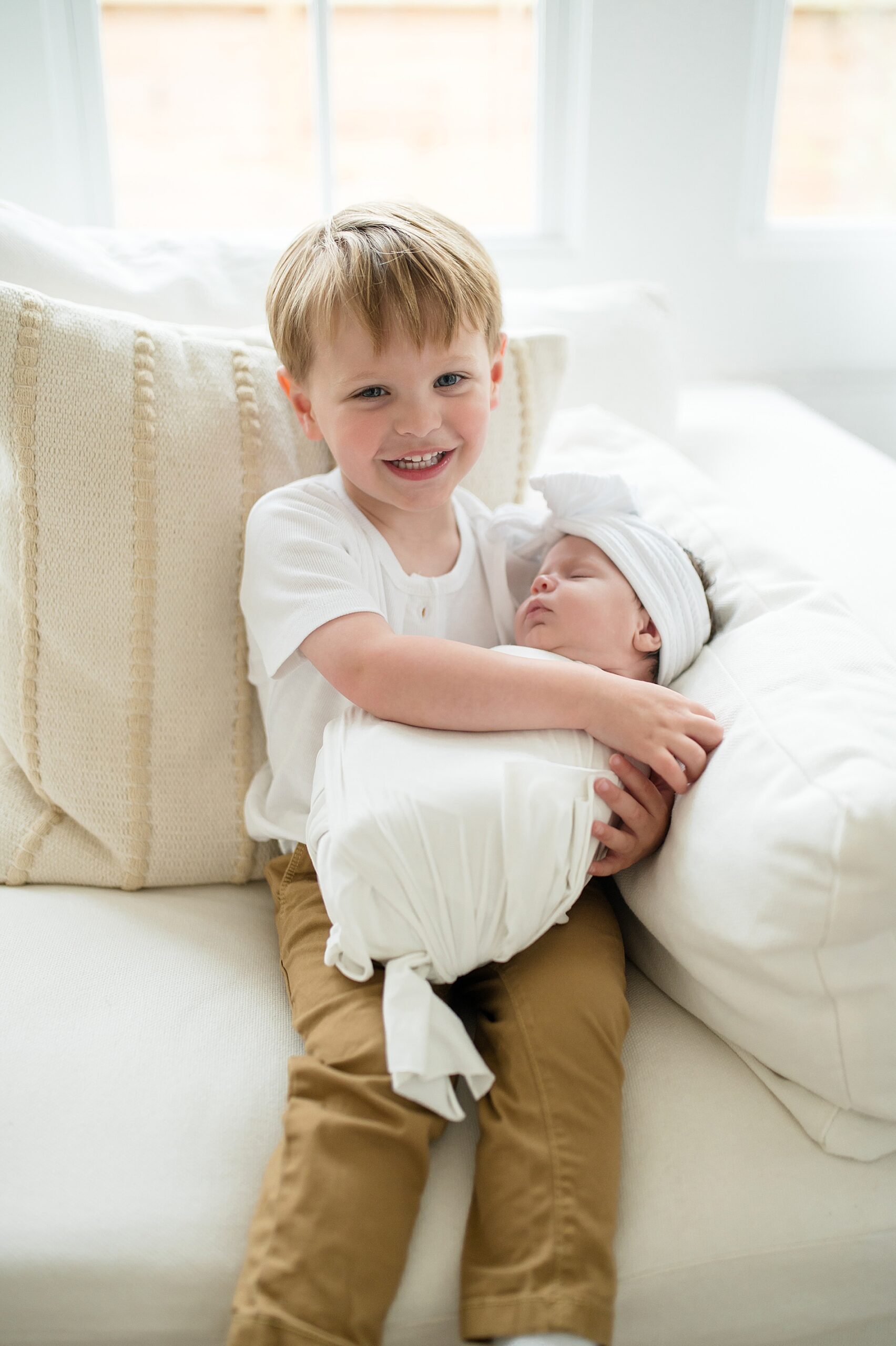 big brother holds his little sister wrapped in white blanket 