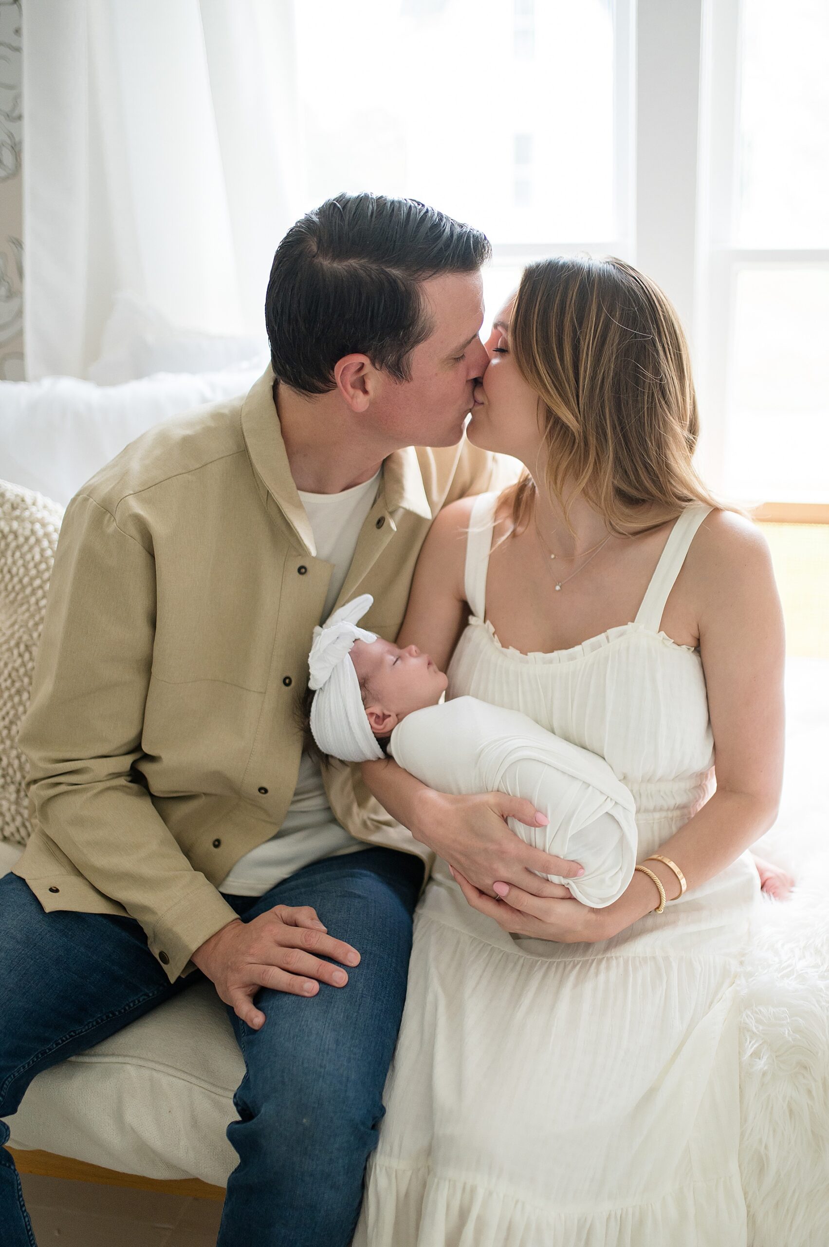 parents kiss as they hold newborn girl
