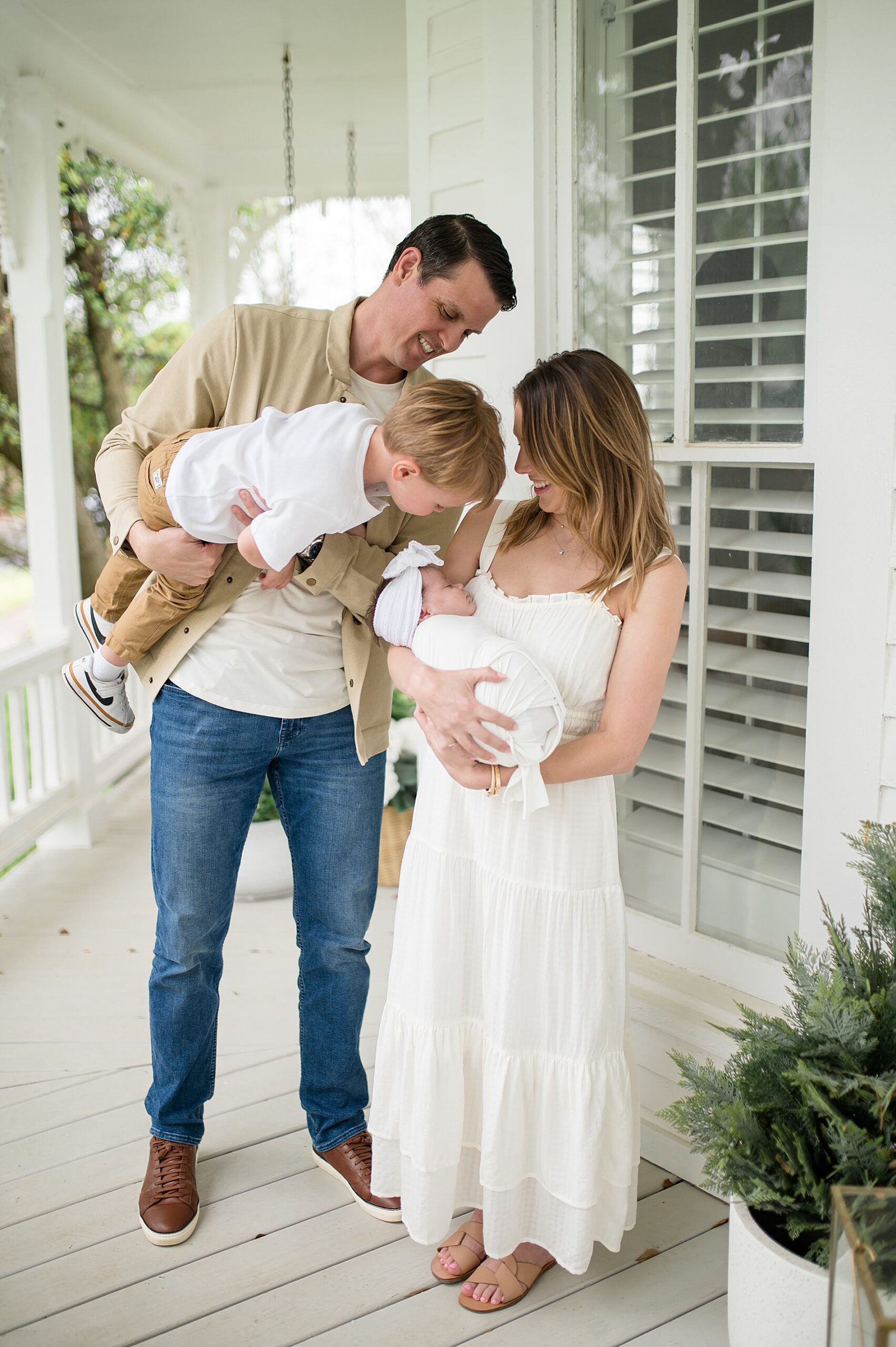 parents hold their children as little boy leans down to kiss newborn sister