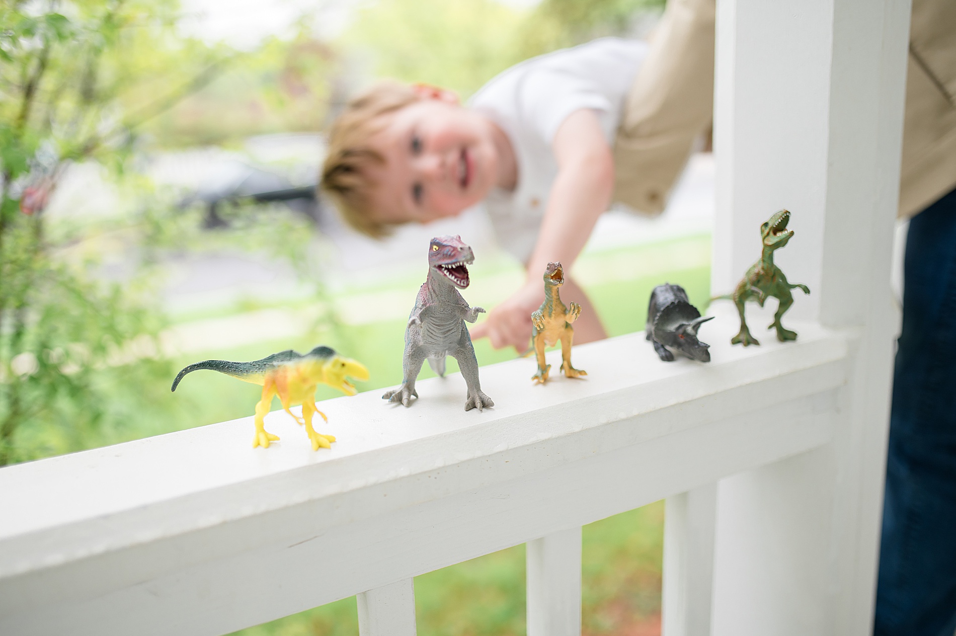baby boy looks at his dinosaurs lined up on porch