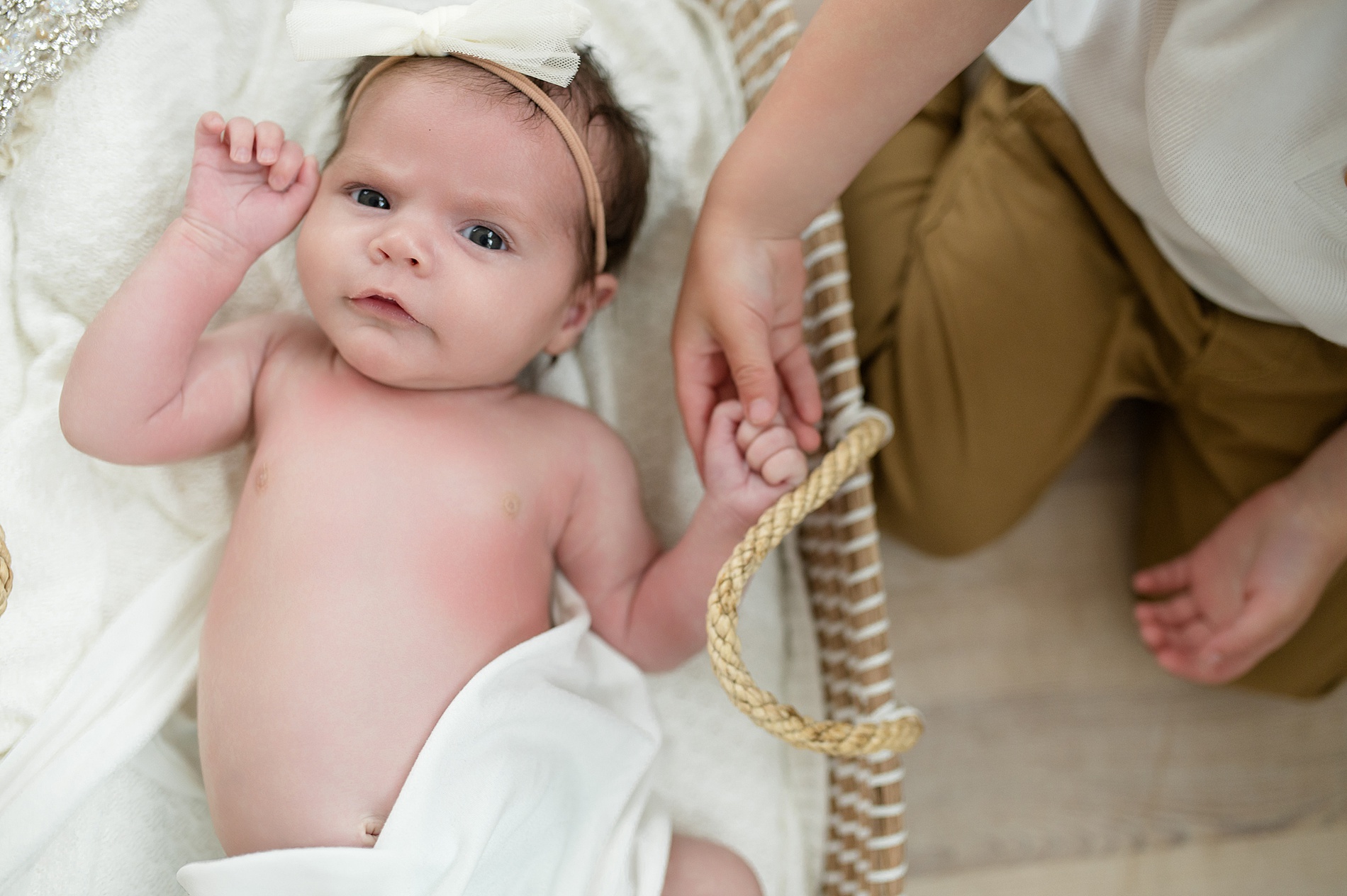 big brother holds newborn sister's hand as she lays in bassinet 