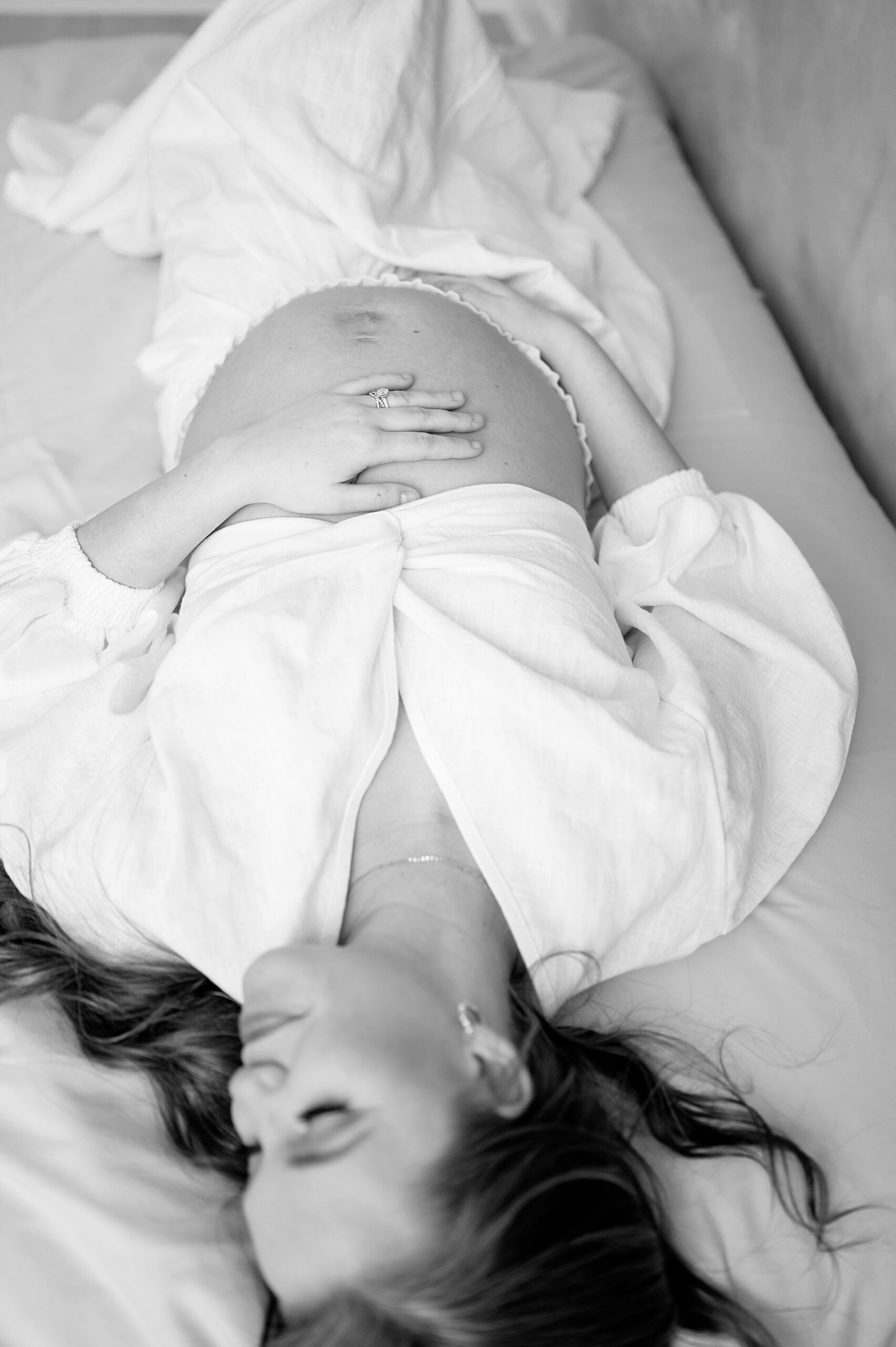 mom lays on bed holding baby bump