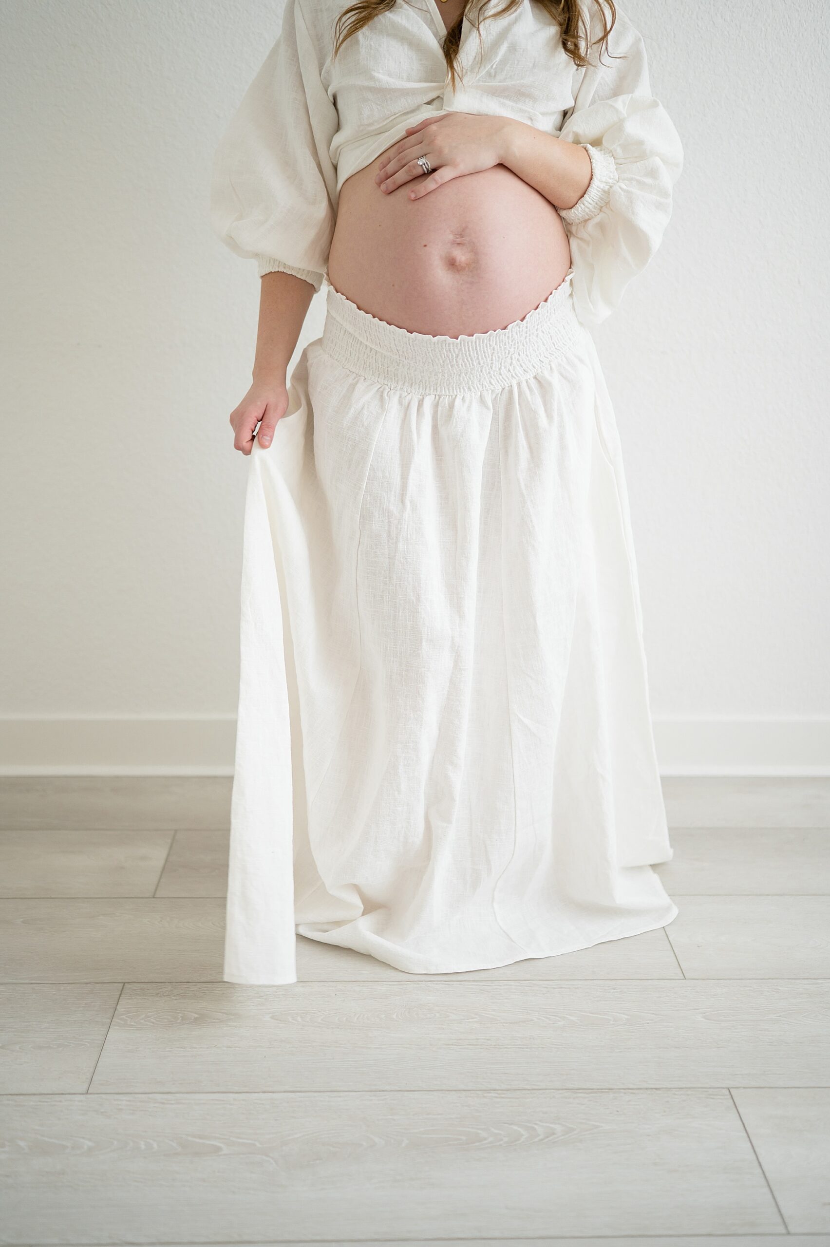 woman in white skirt and shirt showing off pregnant woman's belly