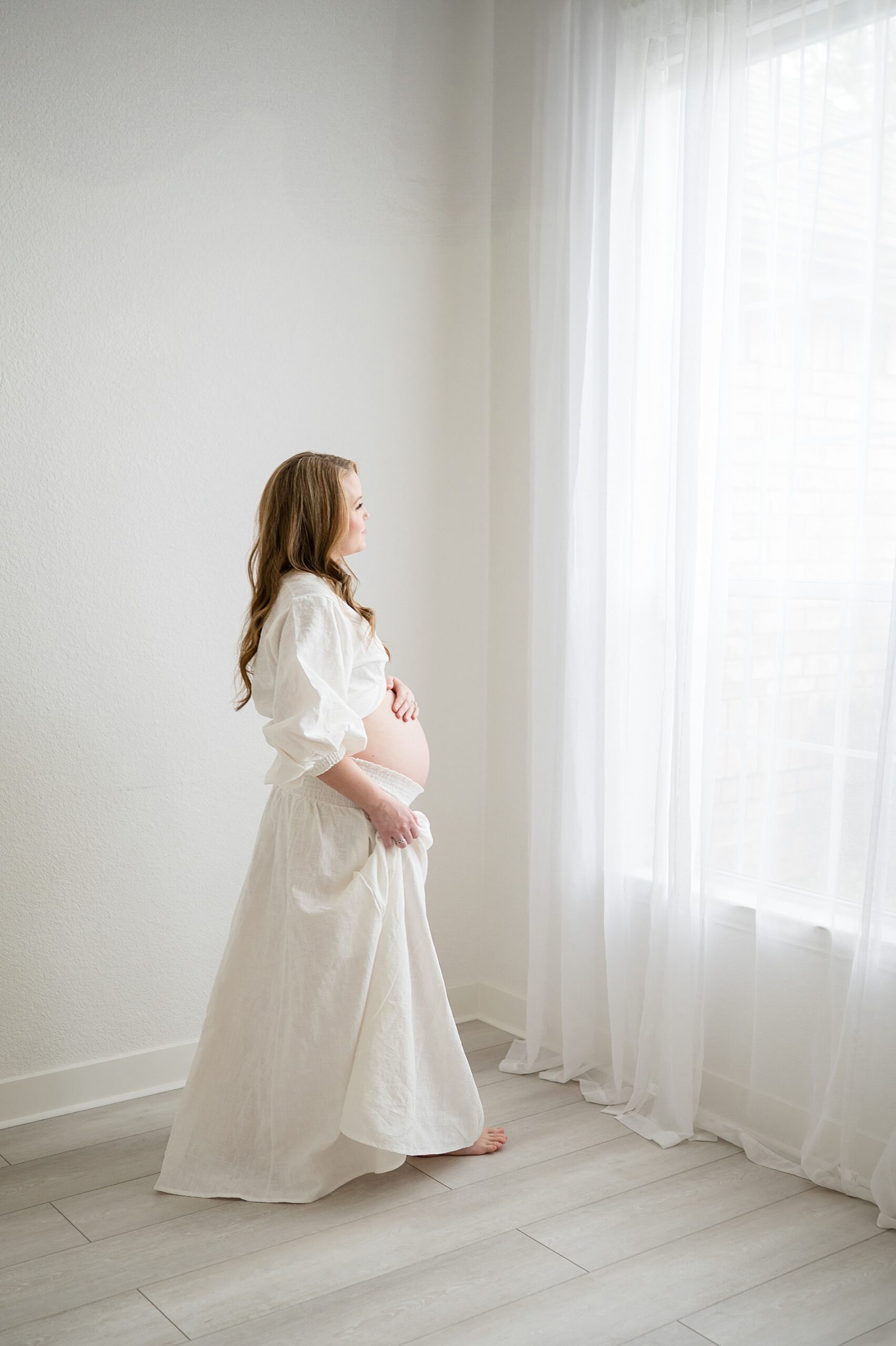 expectant mom looks out window during Intimate Studio Maternity Session
