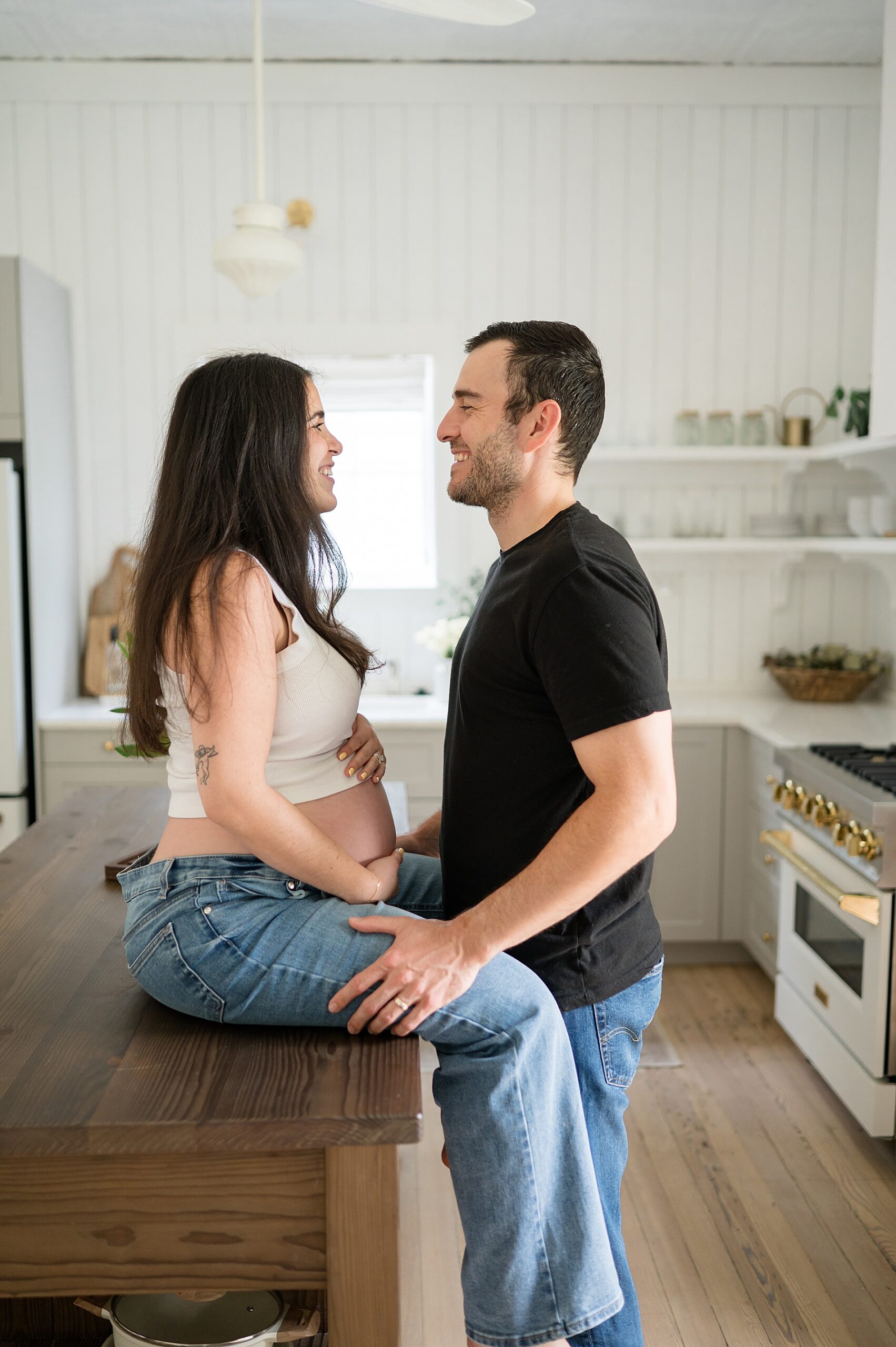 woman sits on counter with husband during maternity photos