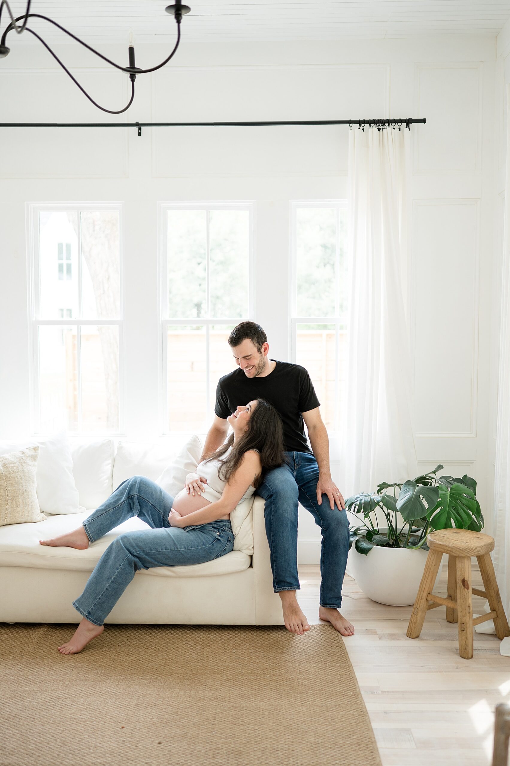 expecting parents sit on couch together during studio maternity session in Dallas