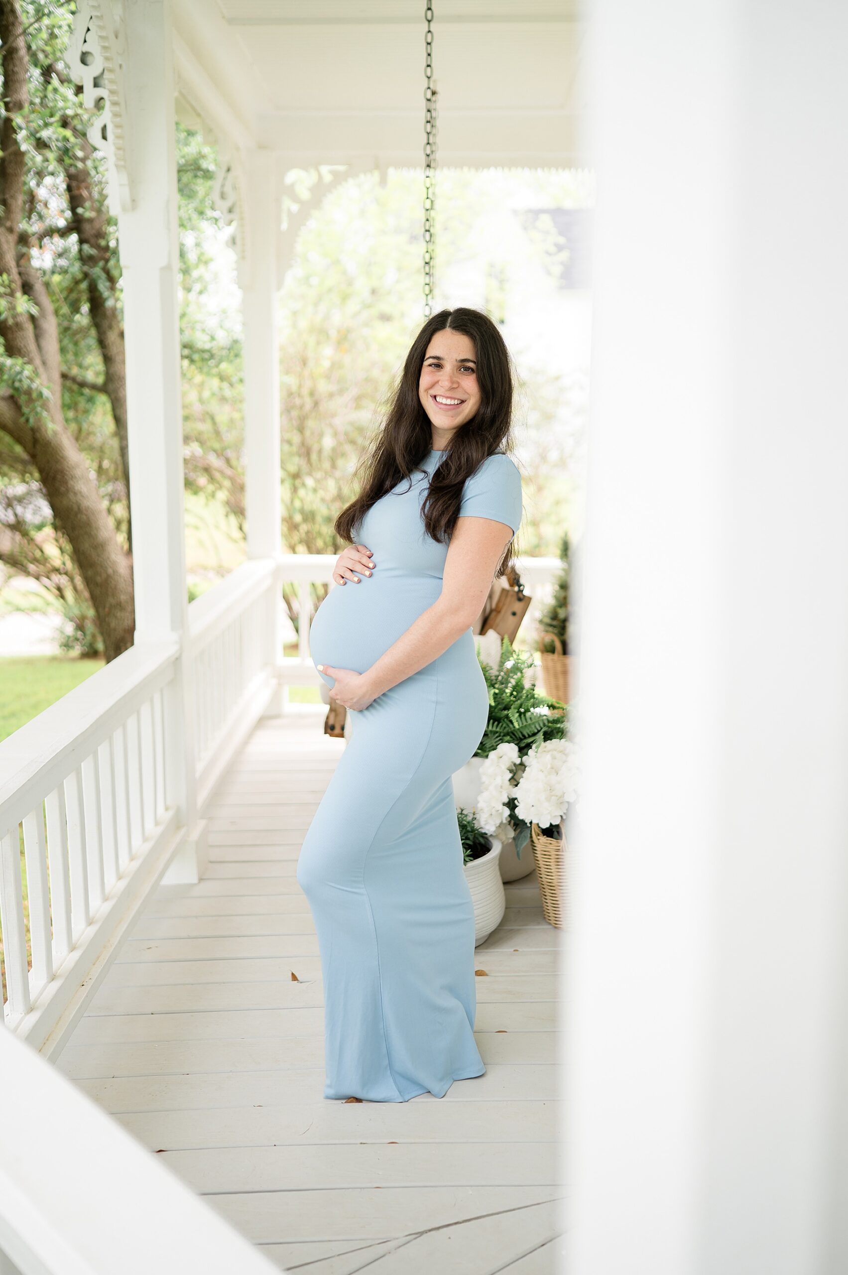 pregnant woman in pale blue dress stands on porch | Why 28-34 weeks is the sweet spot for maternity photos
