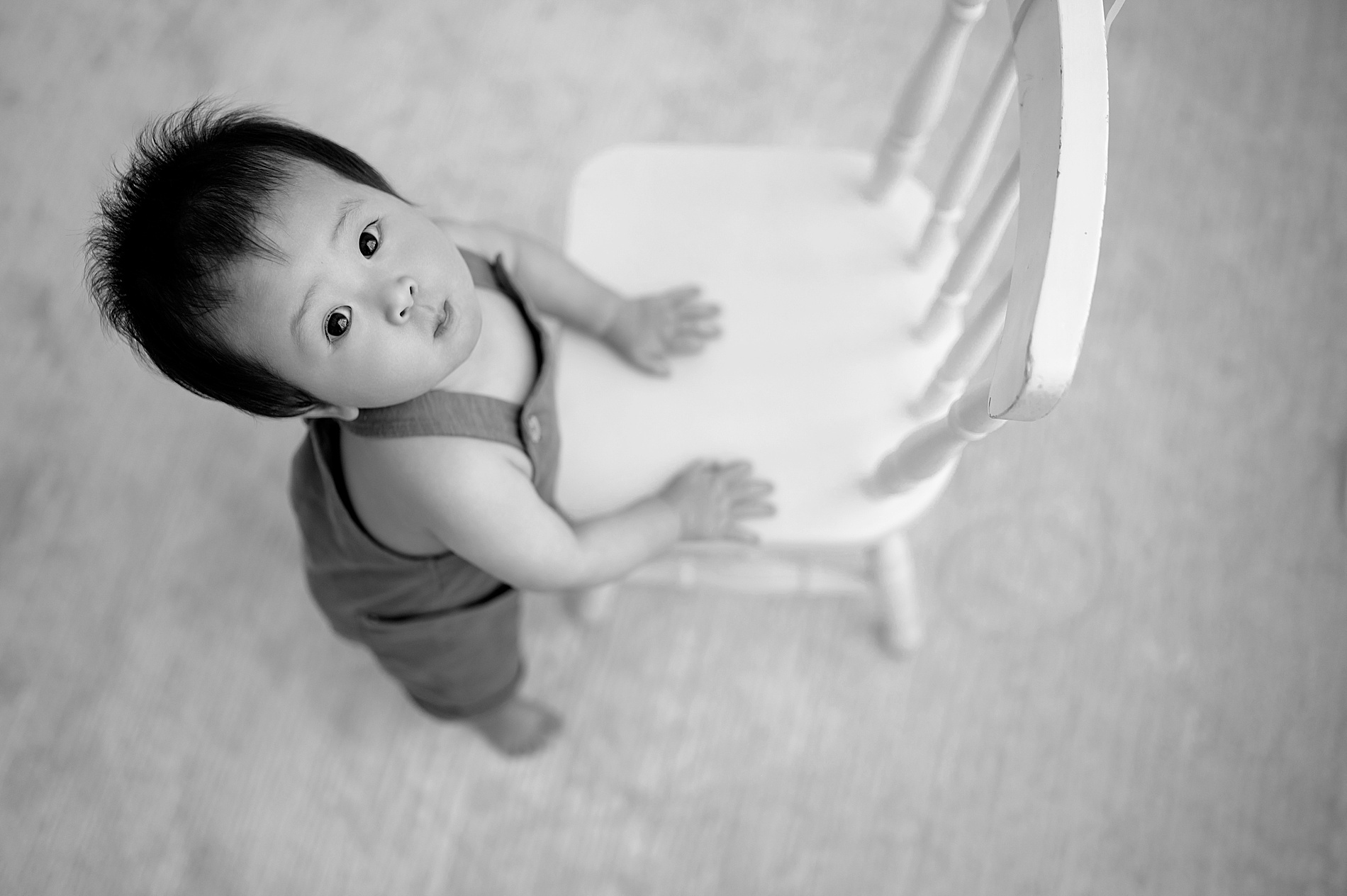 little boy stands while holding on to chair during One Year Milestone session at Dallas studio