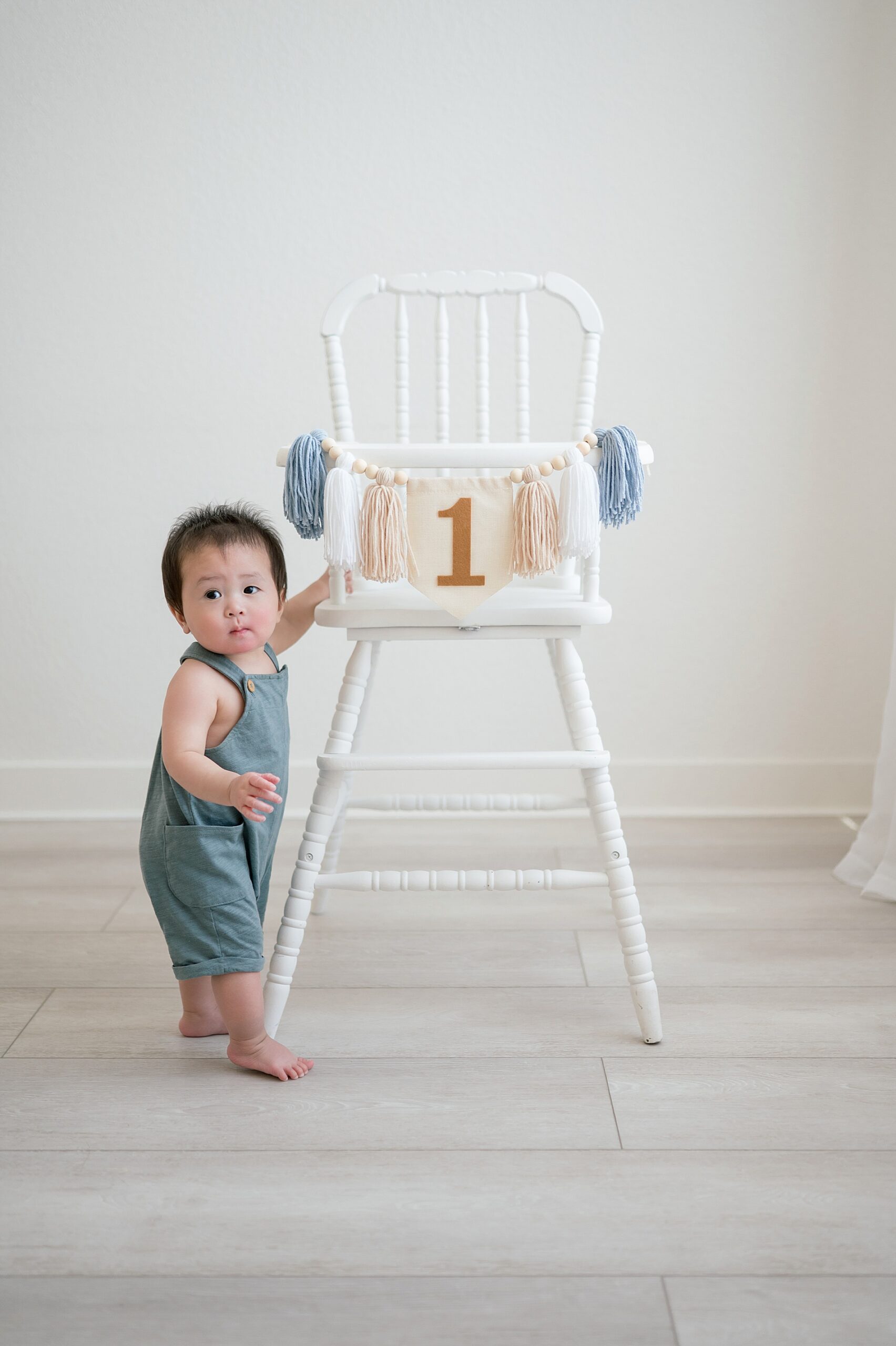 little boy stands by white highchair with first birthday decorations