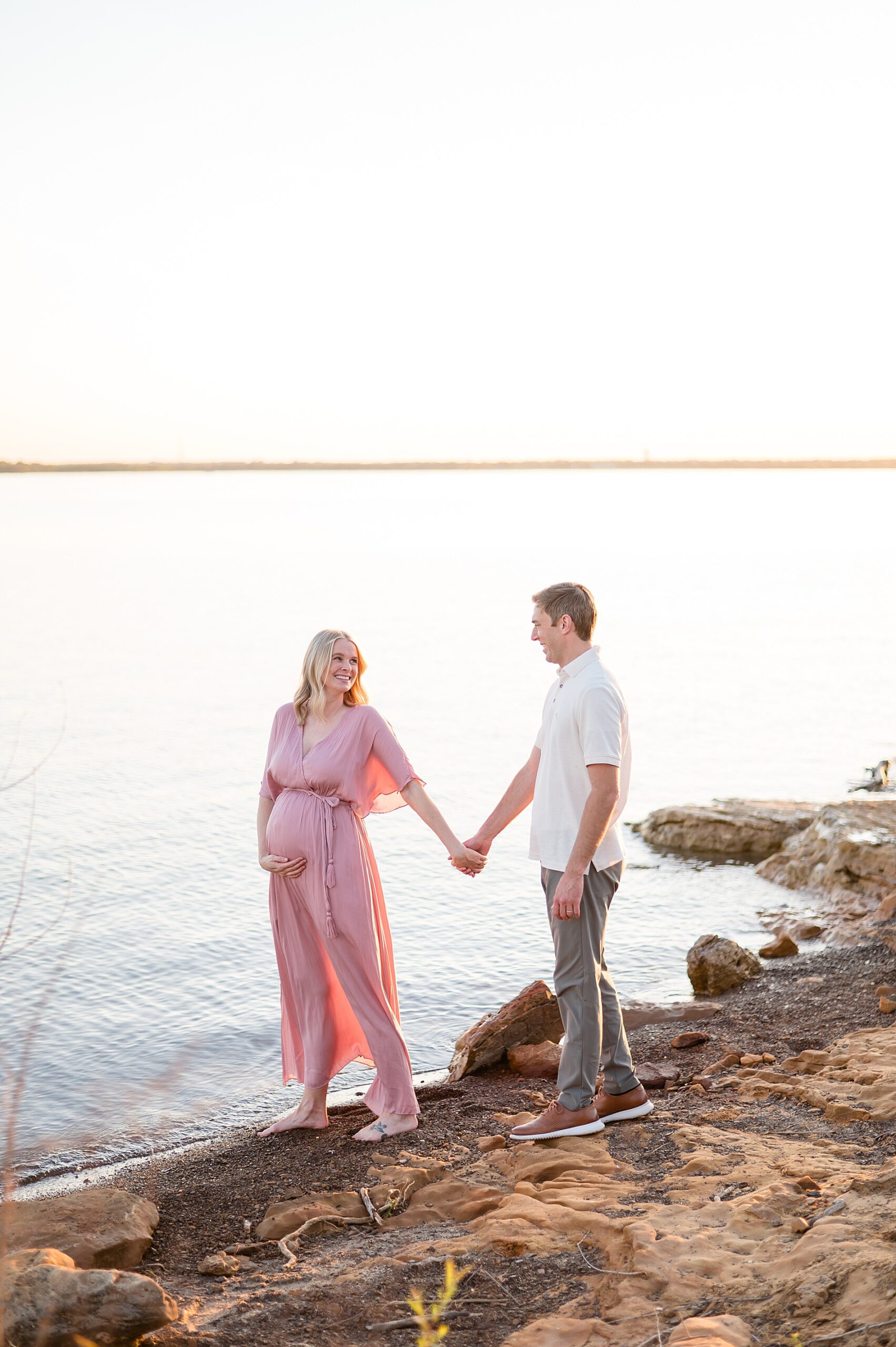 couple hold hands as they walk by the water