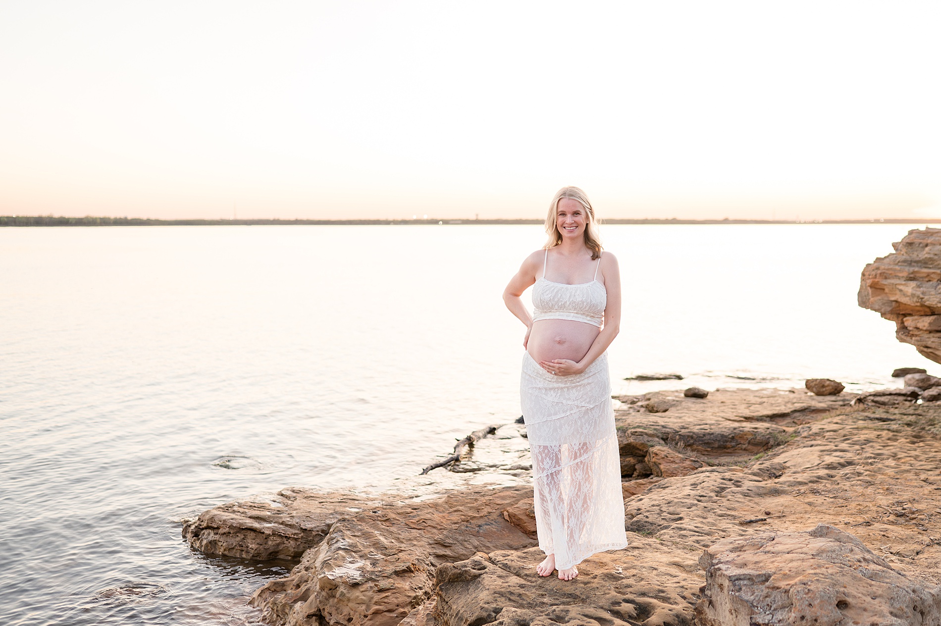 woman places hand on baby bump as she walks along rocky shore