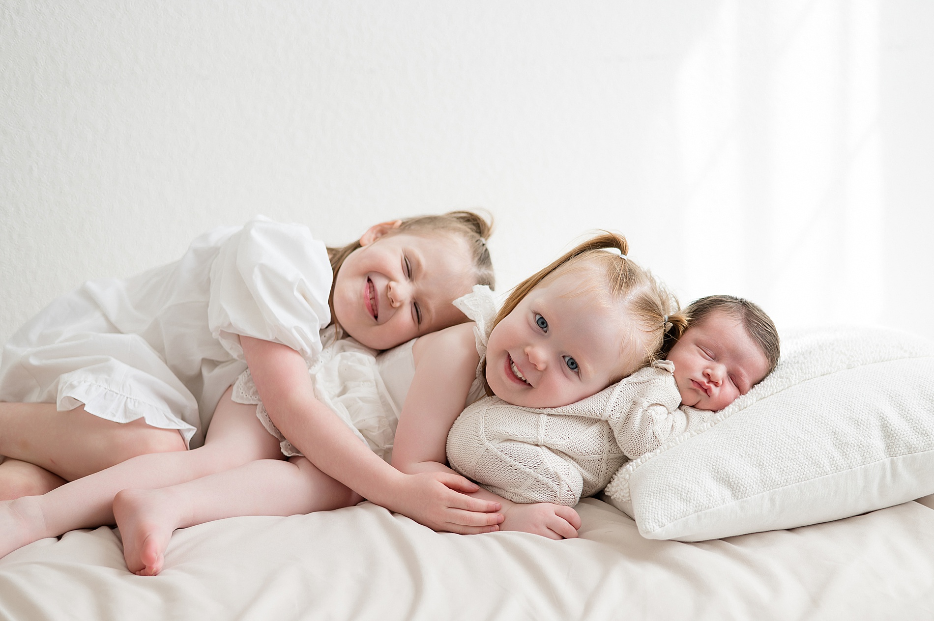 2 older sisters snuggle with baby brother during studio newborn session