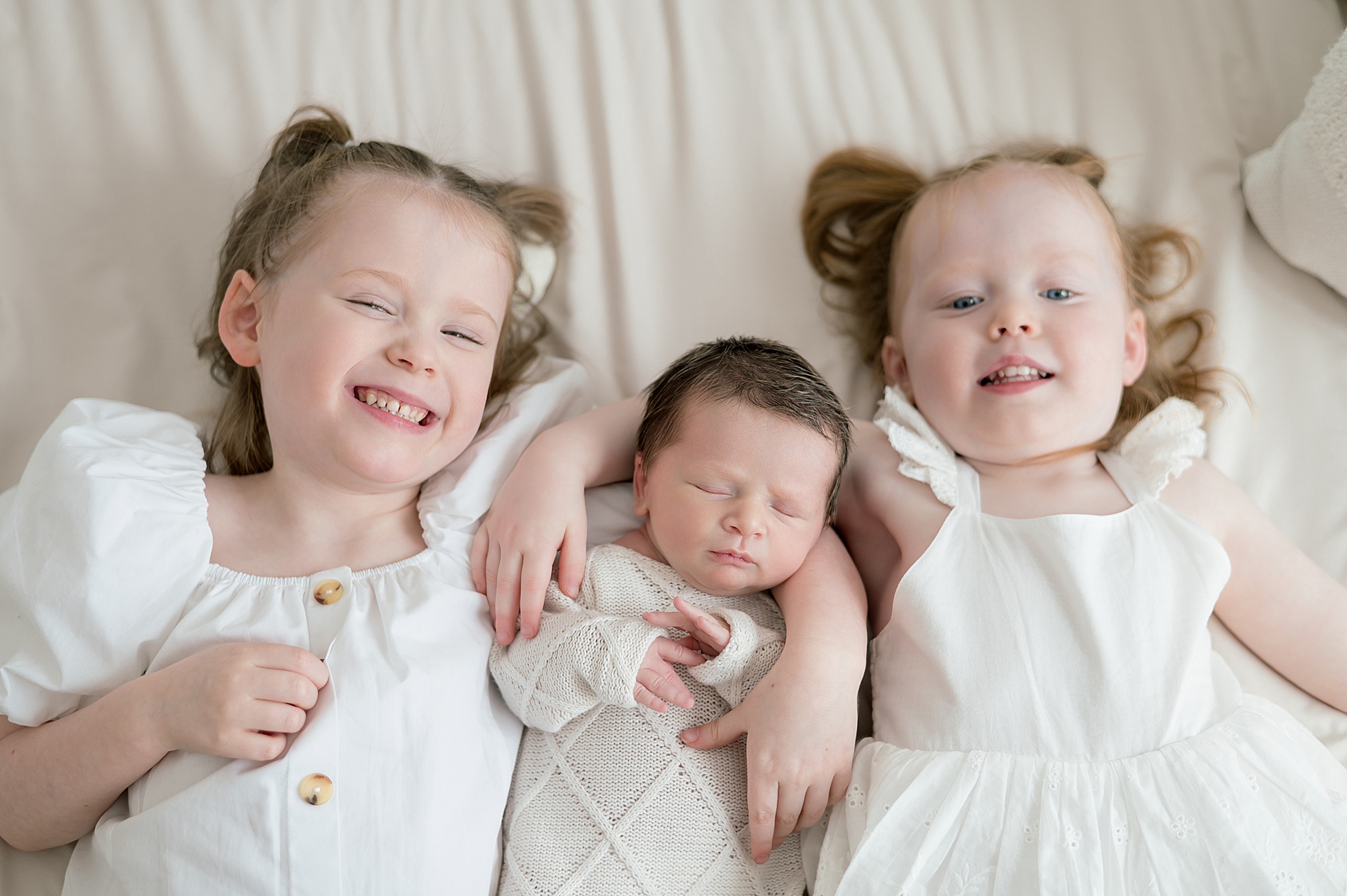 older siblings lay next to baby brother
