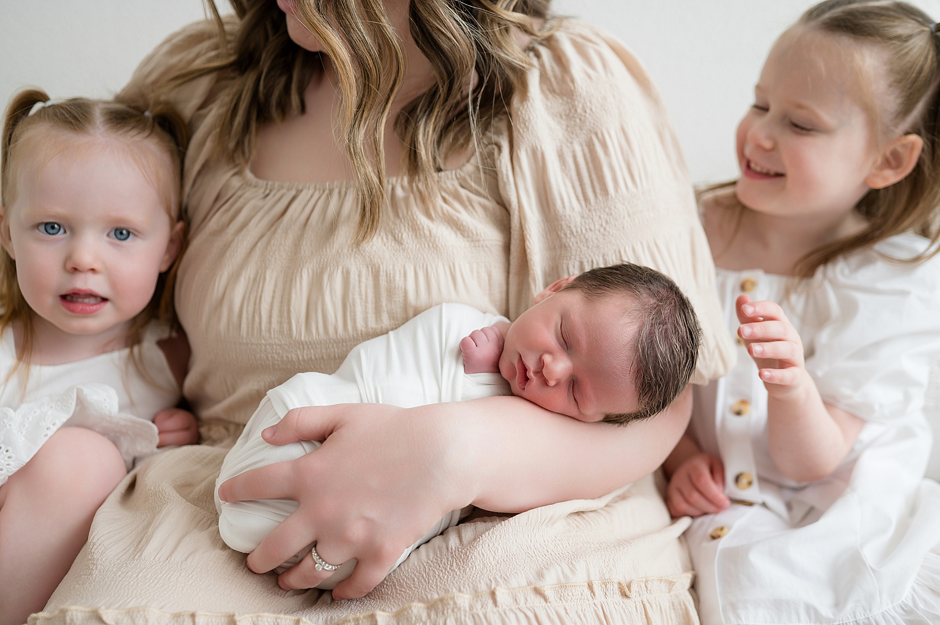 mom holds newborn with big sisters sitting on either side