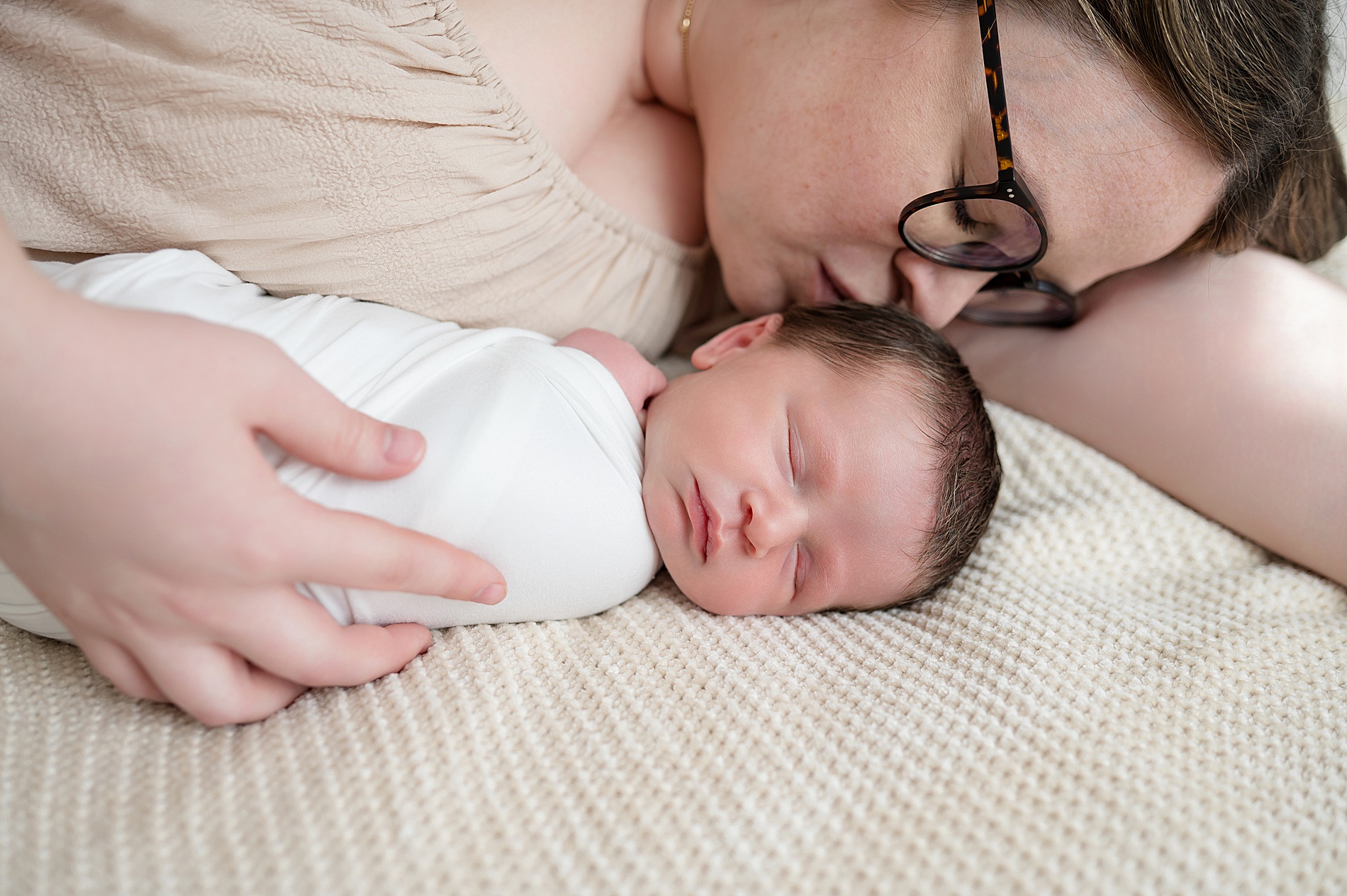 mom lays next to newborn boy and kisses his head