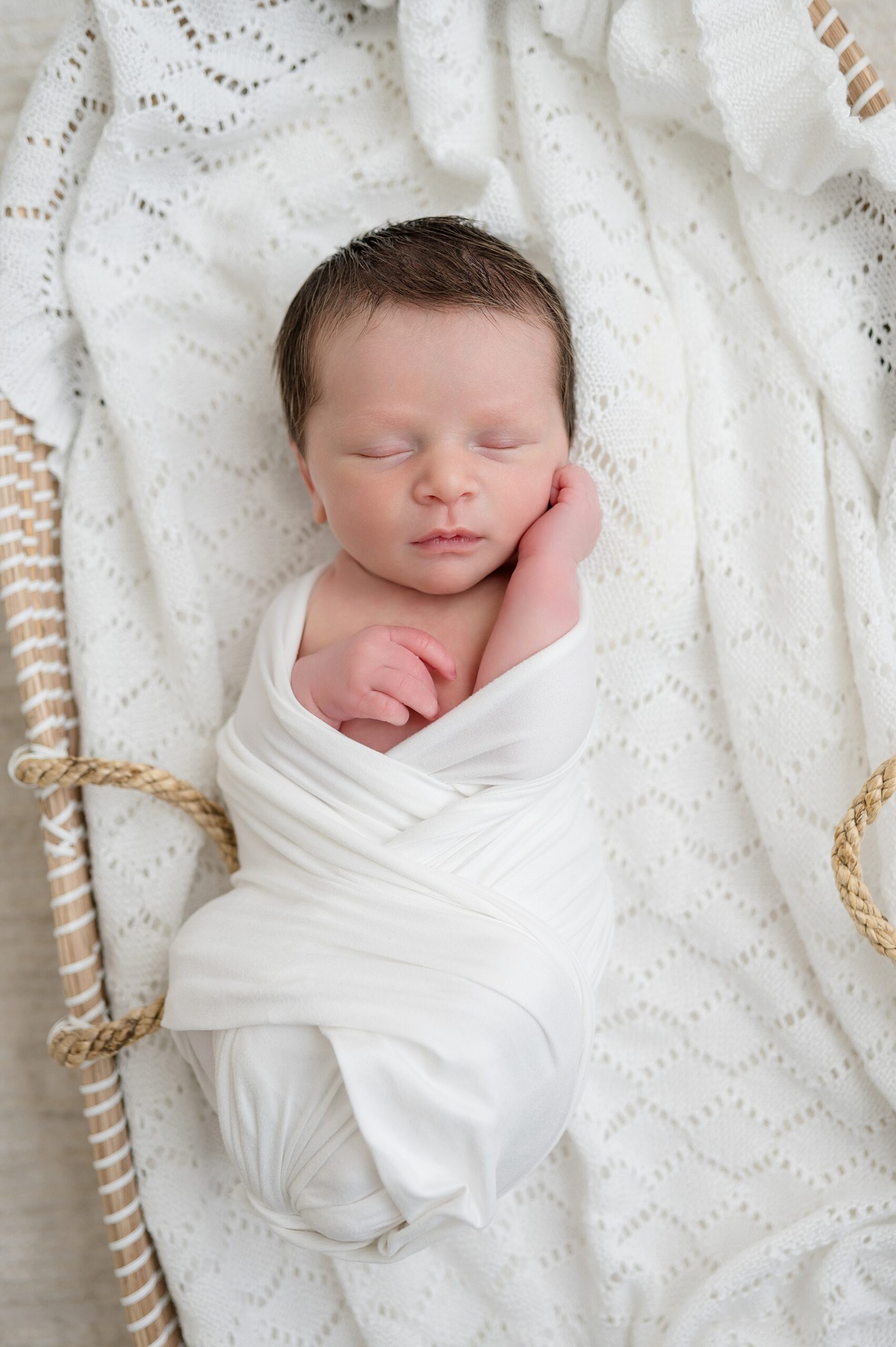 newborn swaddled in white blanket sleeps in bassinet