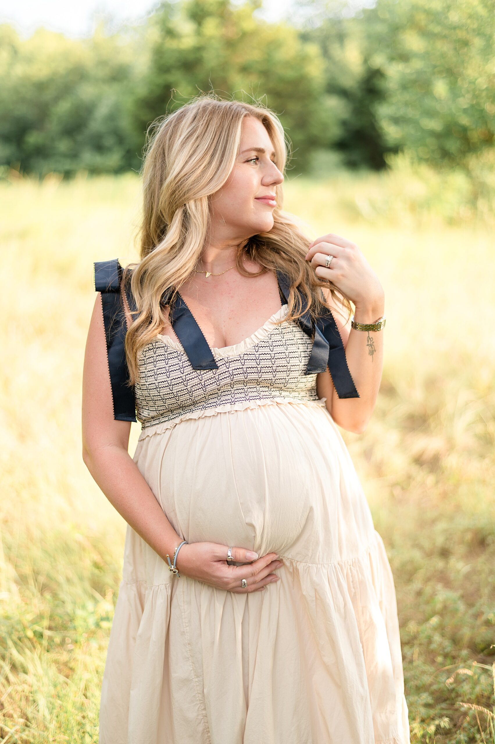 woman in cream dress with black bows on the shoulder during Light and airy maternity session