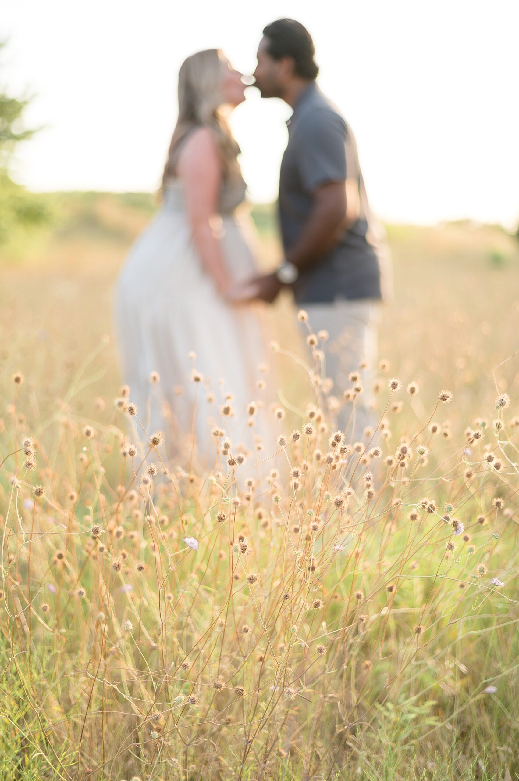 couple kiss in field during Dallas maternity session