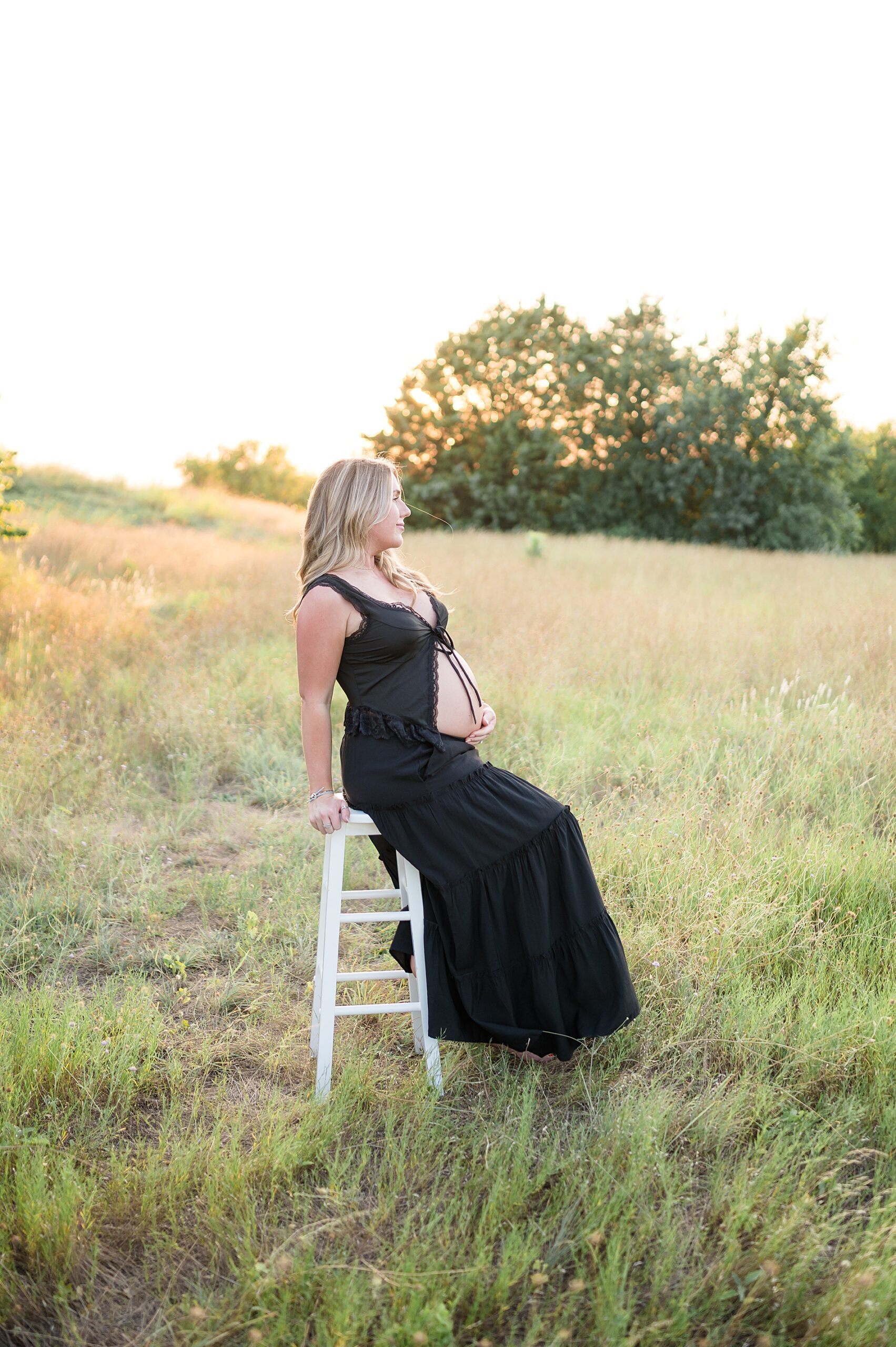 Pregnant woman sits on white stool in grassy field