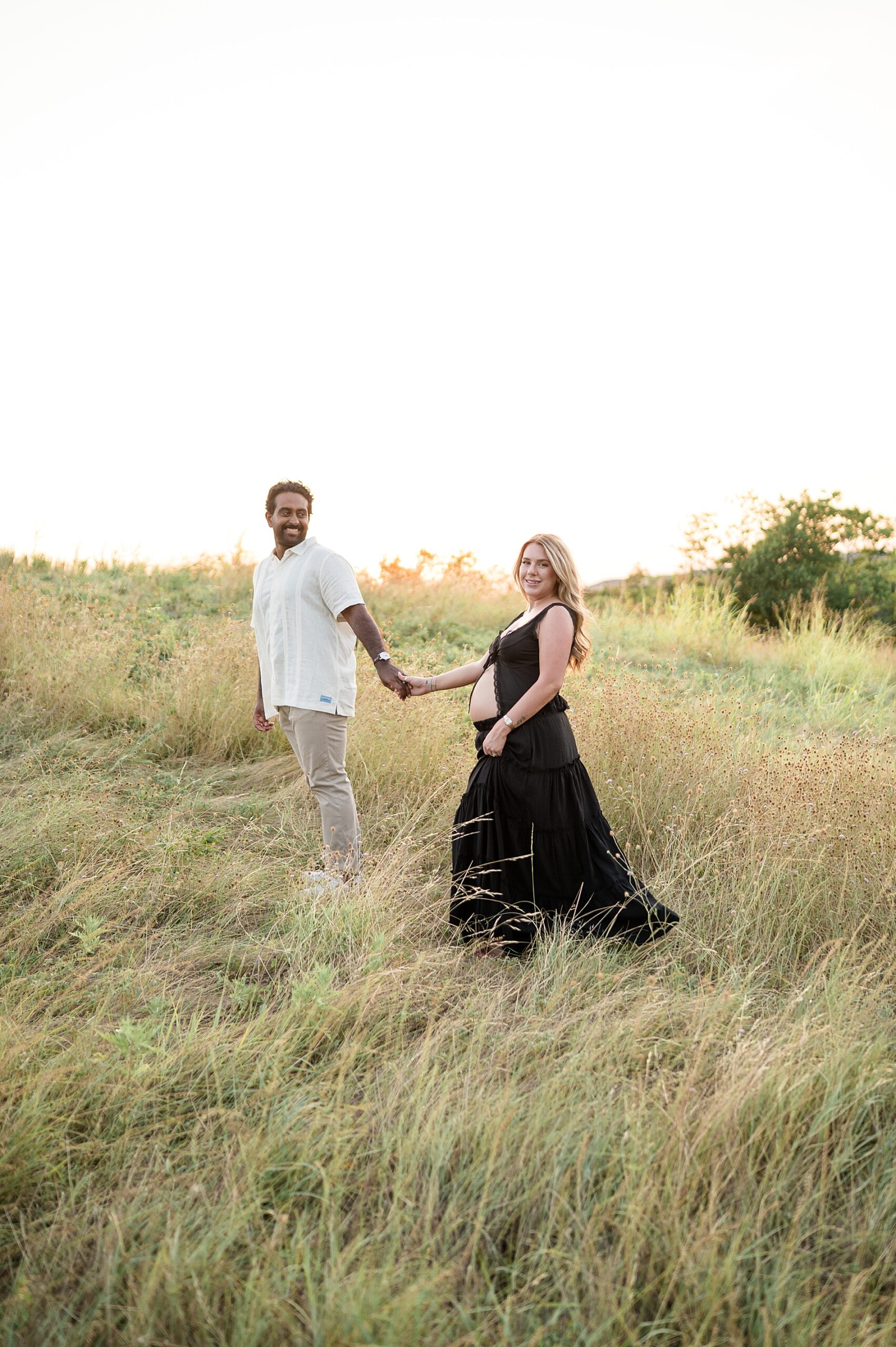 couple hold hands as they walk through tall grass 