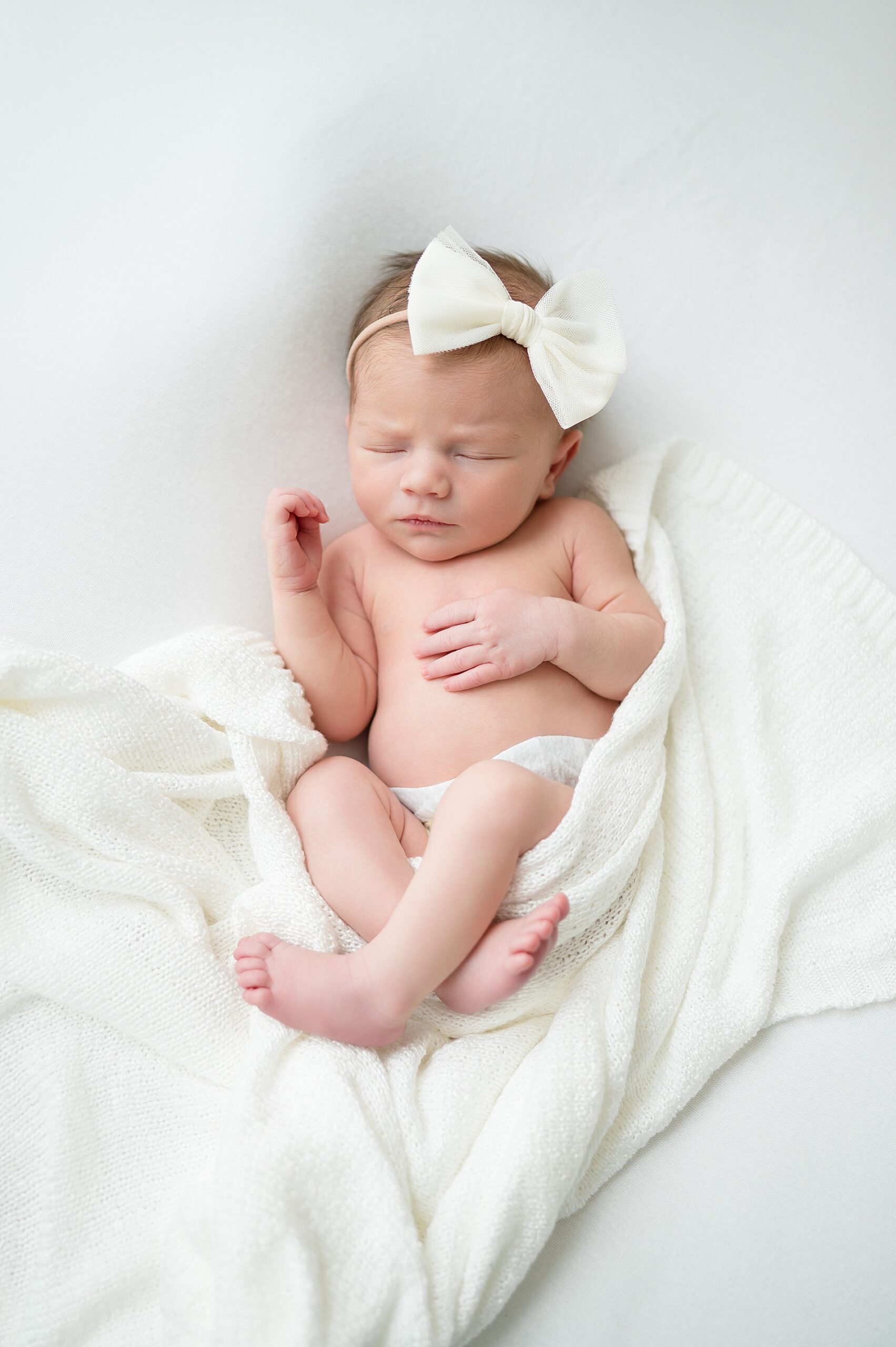 newborn girl sleeping with white bow during studio newborn session