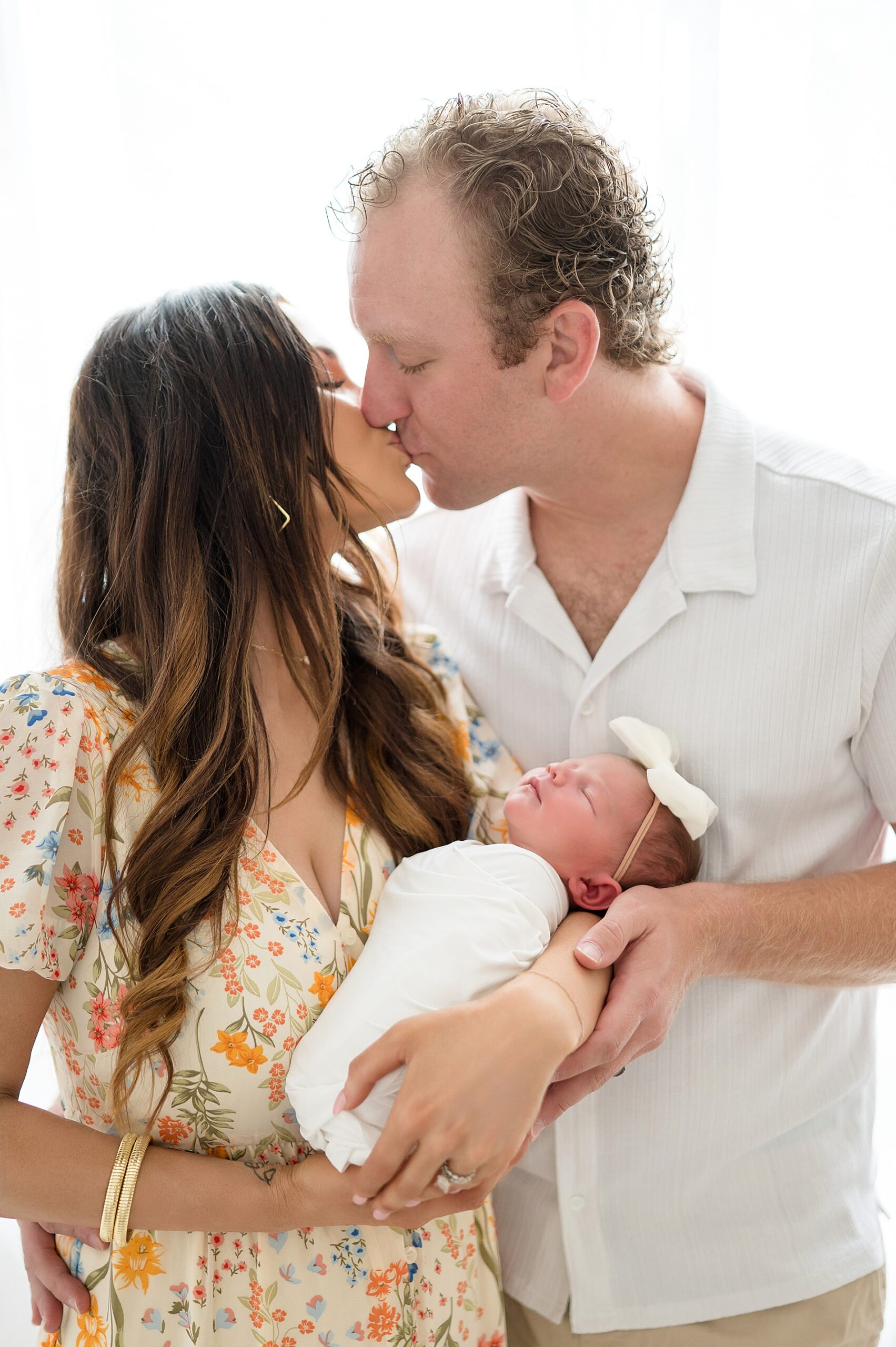 parents kiss as they hold newborn girl