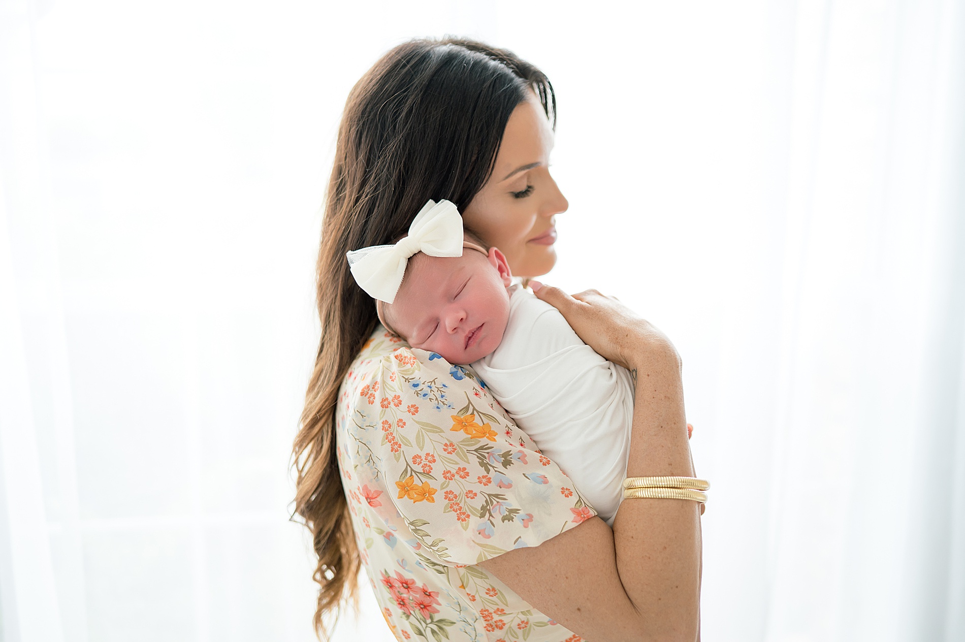 mom holds newborn girl by window