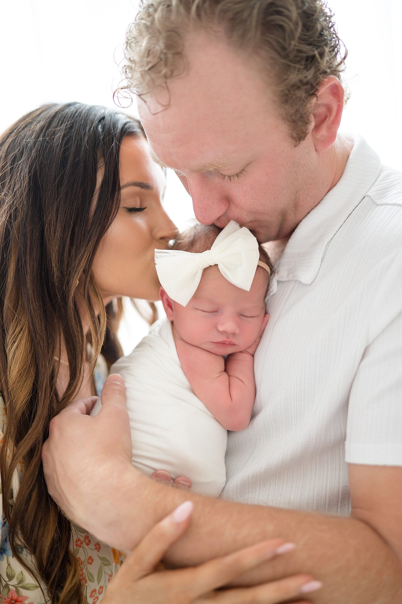 both parents kiss newborn's head while dad holds her during | Studio Newborn Photography by Little elm newborn photographer
