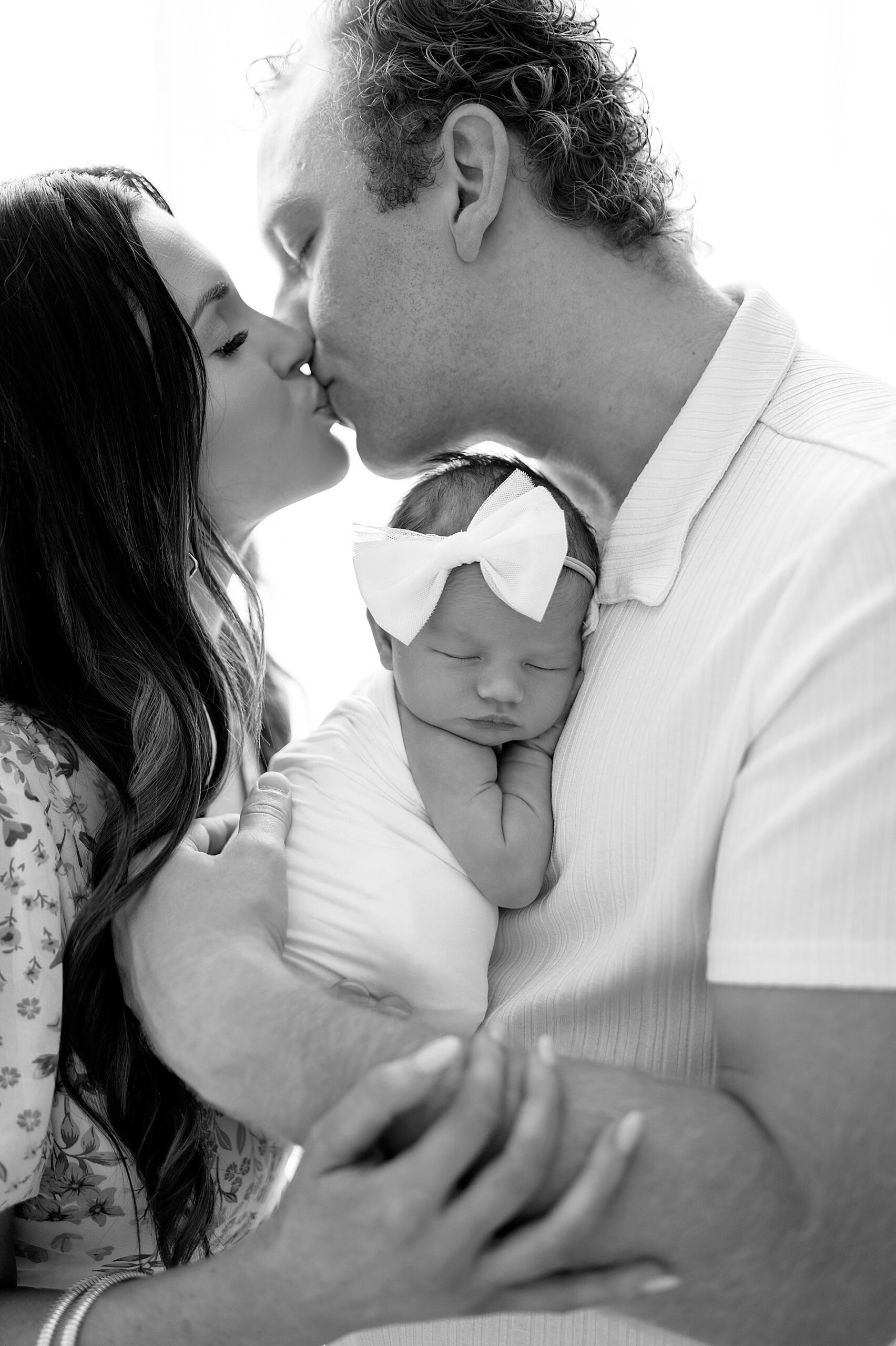 parents kiss while holding newborn